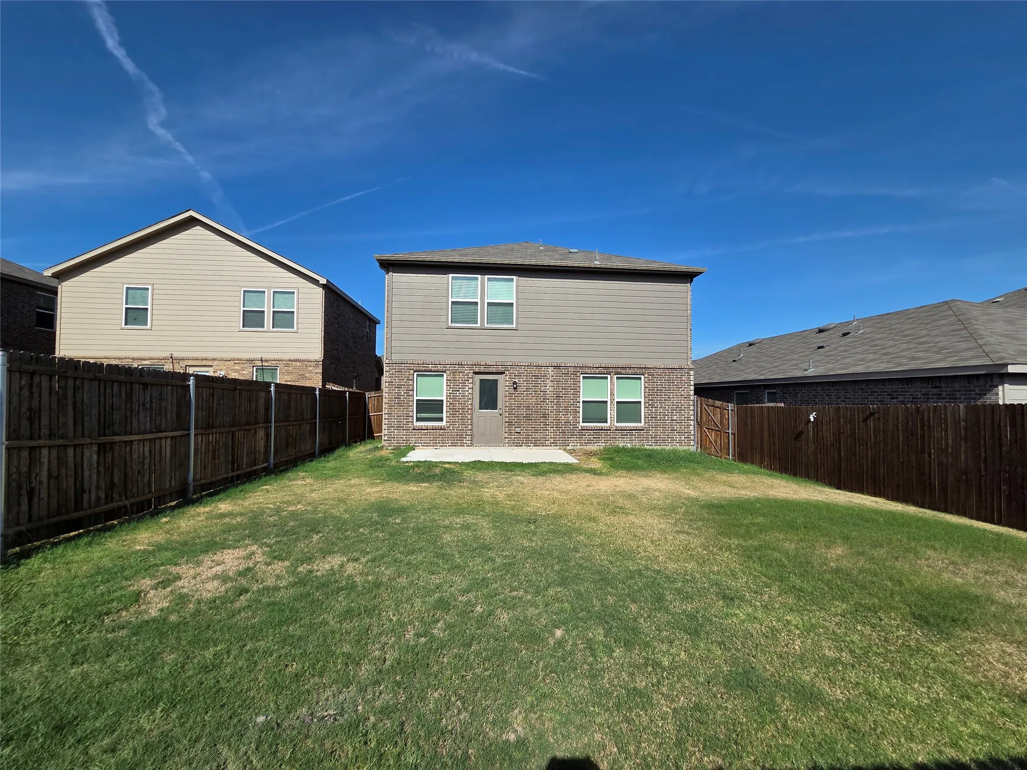 Expansive backyard with a wood privacy fence, concrete patio, and a two-story exterior featuring brick and horizontal siding