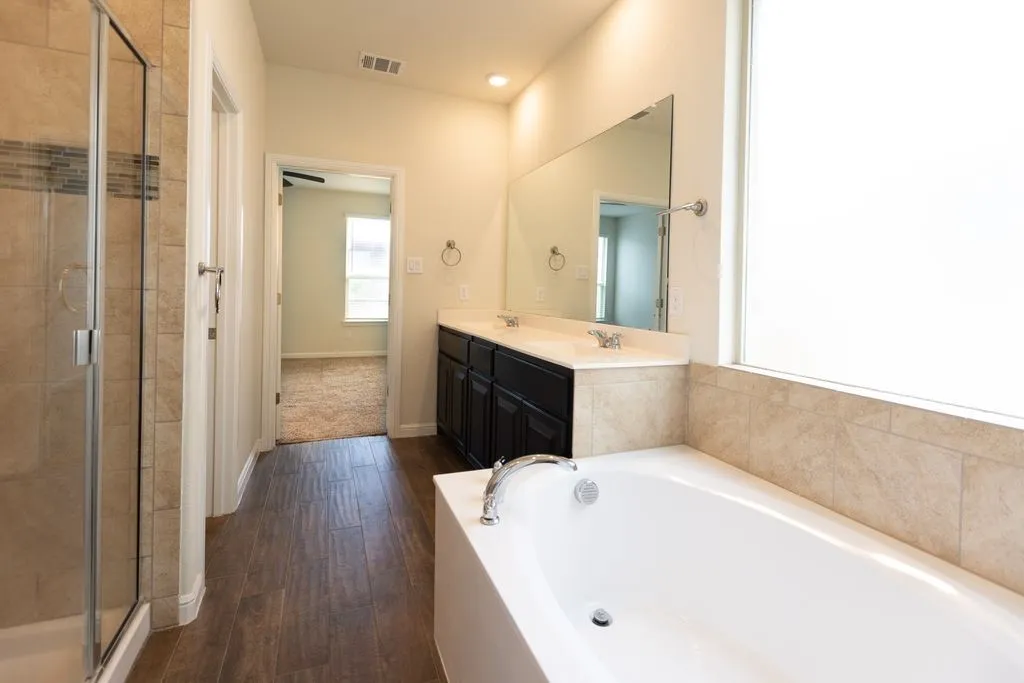 Spacious bathroom featuring a glass-enclosed shower, dual vanity, soaking tub, and tile-finish flooring