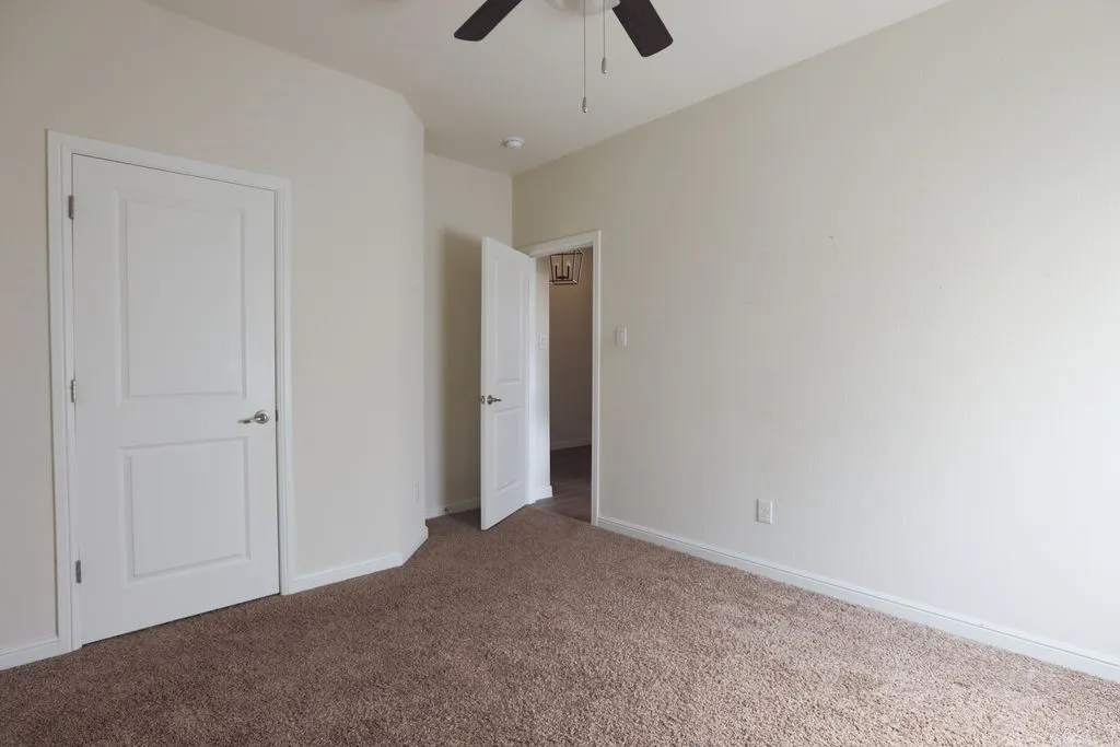 Brown carpeted flooring with white baseboards, white walls, and a ceiling fan