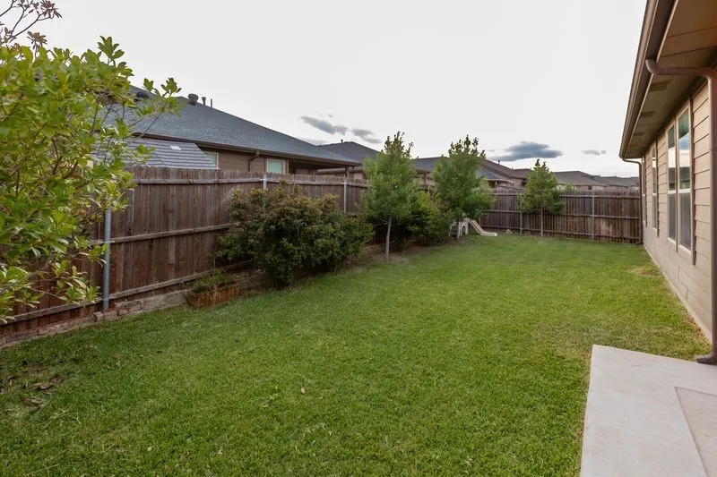 Expansive green lawn with mature trees and shrubs, bordered by a wood privacy fence