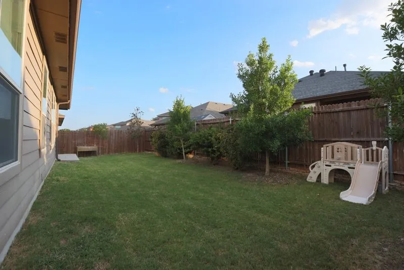 Expansive backyard featuring a manicured lawn, established trees, and a wooden privacy fence