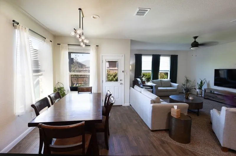 Open-concept living and dining areas featuring wood-finish flooring, a contemporary linear chandelier, and ample natural light