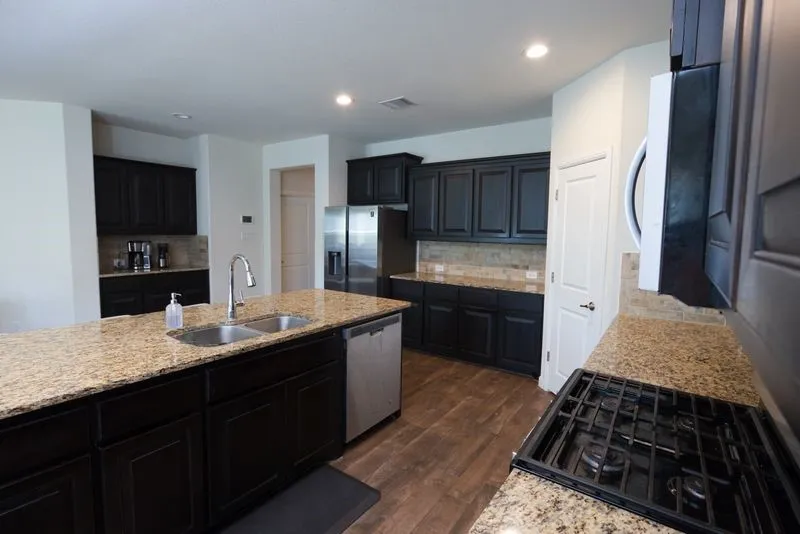 Kitchen featuring dark wood cabinetry, light-toned granite countertops, a built-in gas range, and wood-finish flooring