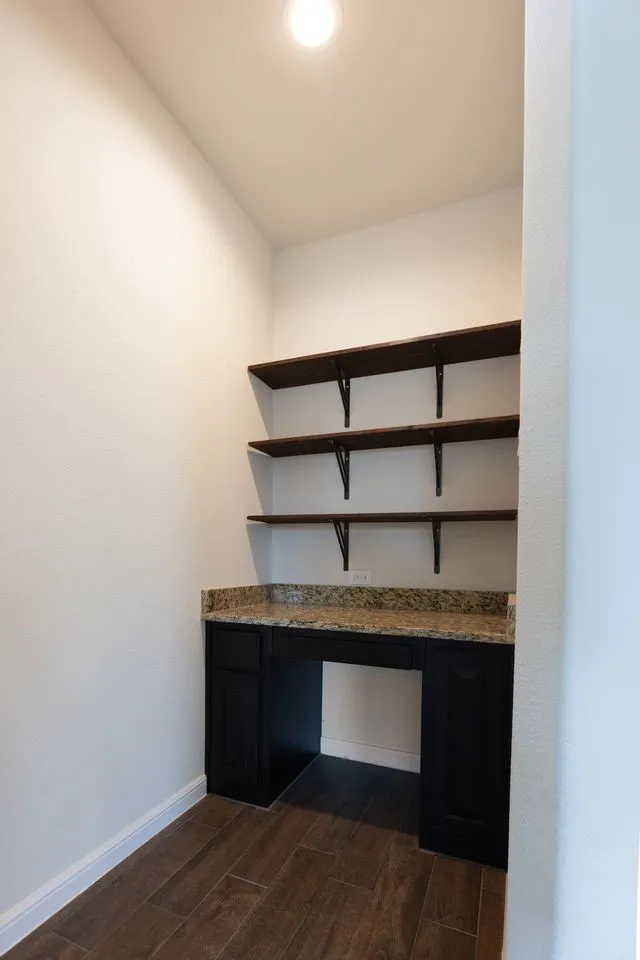 Built-in desk with dark cabinetry, granite countertop, wood-finish flooring, recessed lighting, and wall-mounted shelving