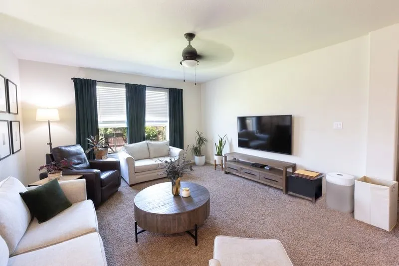Carpeted living space featuring multiple windows with blinds, a ceiling fan, and ample wall space