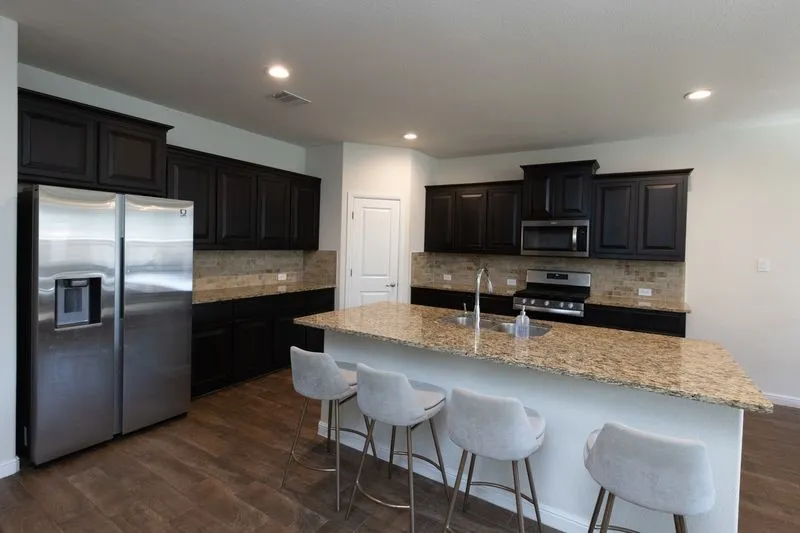 Kitchen featuring dark wood cabinetry, granite countertops, tile backsplash, stainless steel appliances, and wood-finish flooring