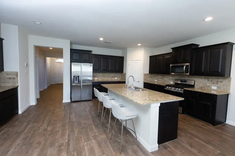 Expansive kitchen island, granite countertops, tile backsplash, stainless steel appliances, and wood-finish flooring