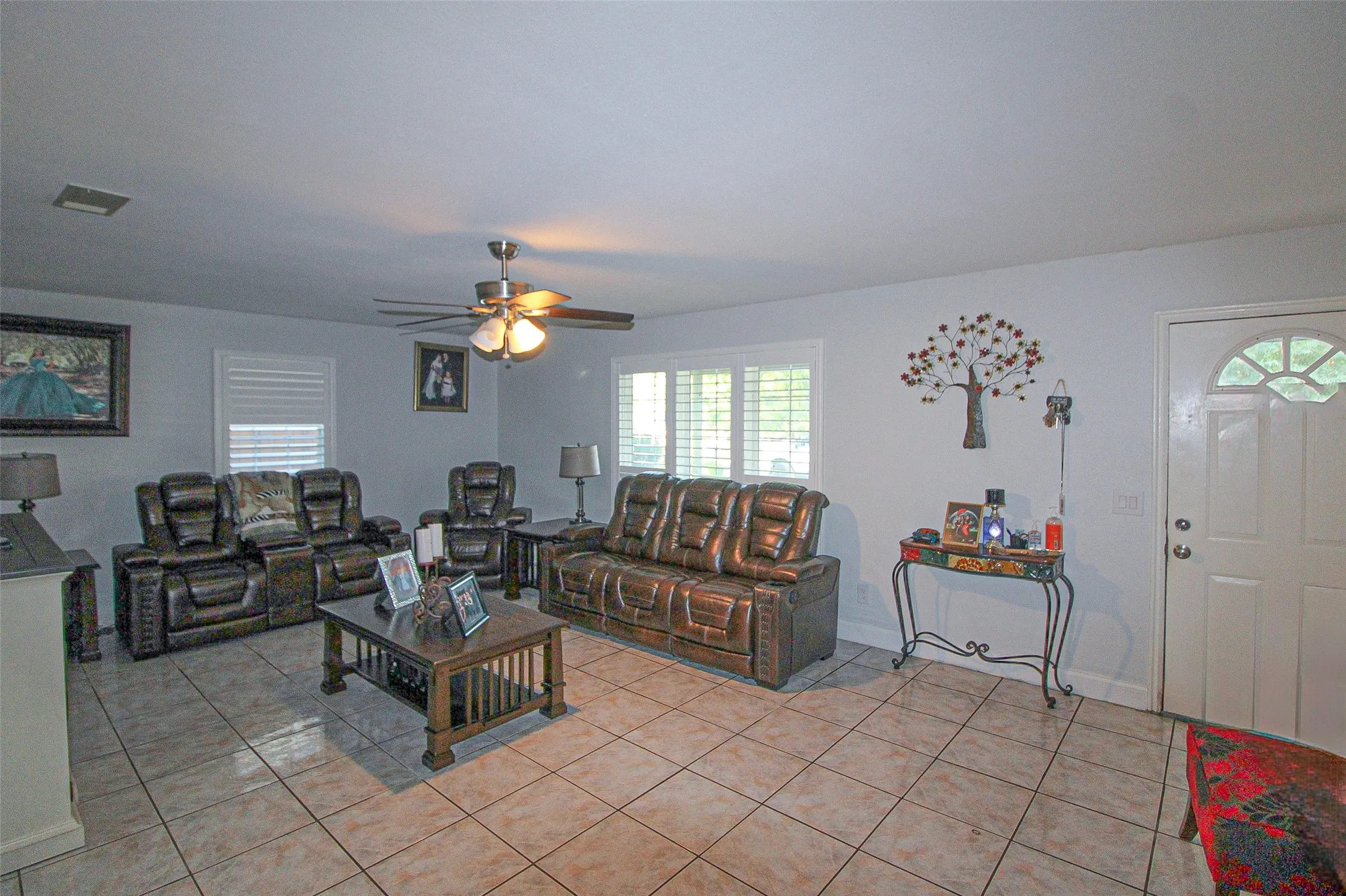 Tile flooring, ceiling fan with integrated lighting, multiple windows with horizontal blinds, and a paneled entry door with an arched window