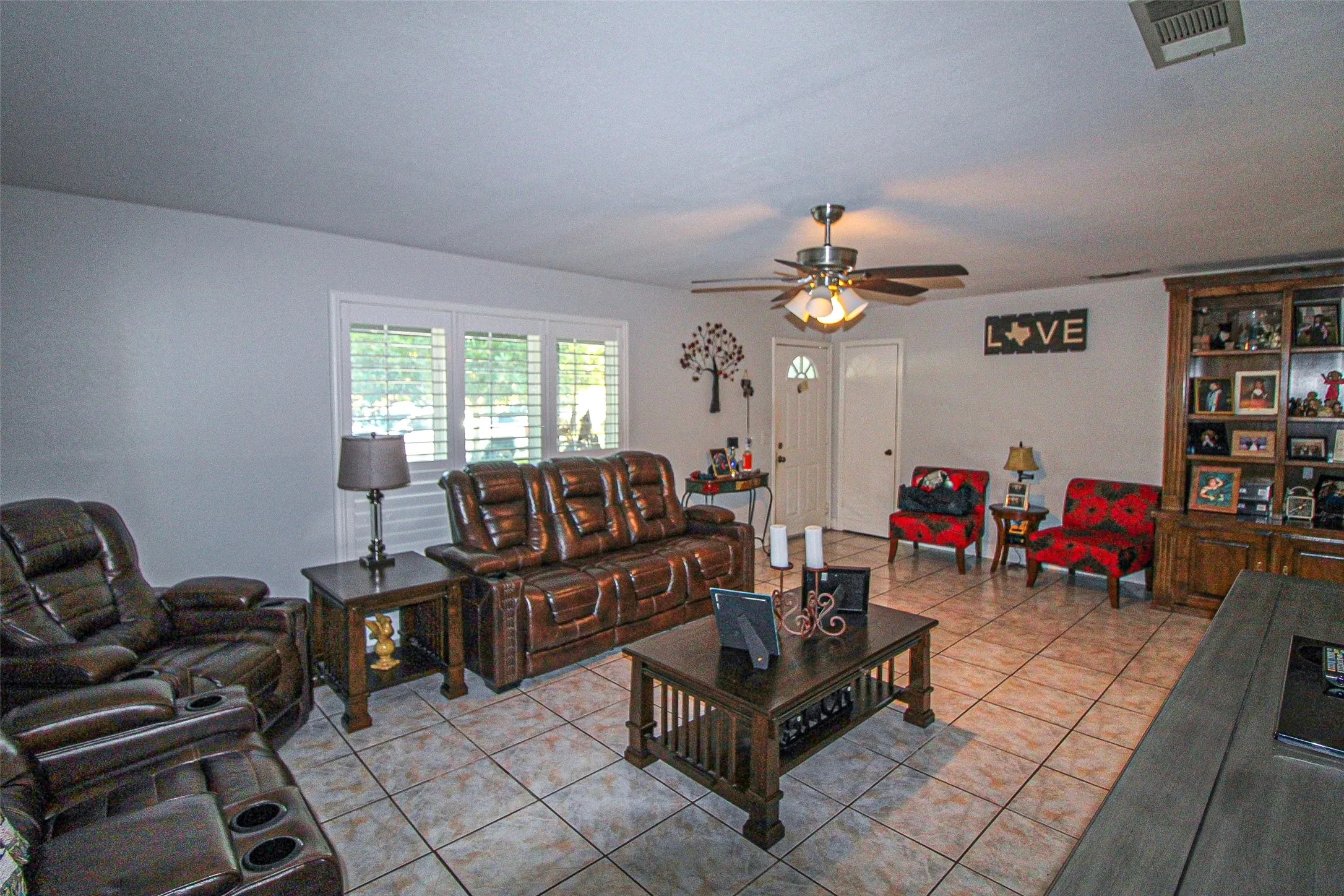 Neutral wall tones, tile flooring, window with plantation shutters, ceiling fan with light fixture, and a built-in display cabinet