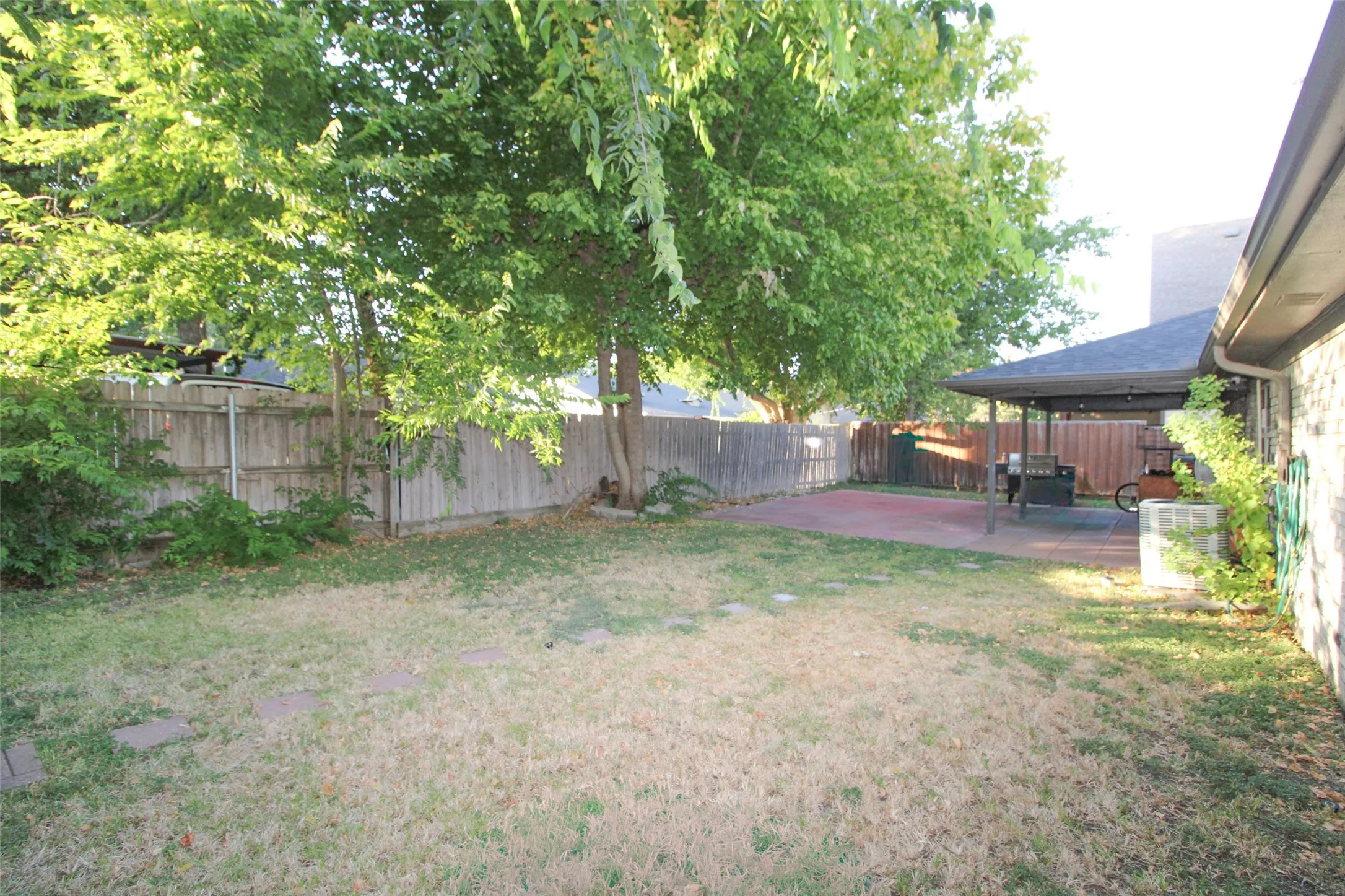 Expansive backyard featuring a covered patio with a concrete slab, a wood privacy fence, and mature trees