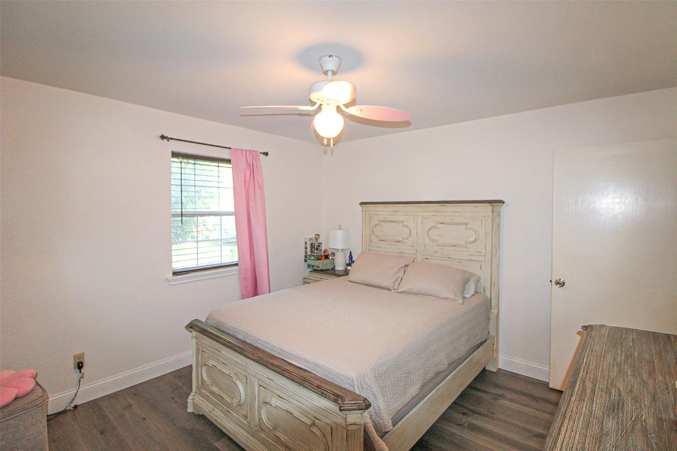 Wood-finish flooring with white baseboards, a white ceiling fan with integrated lighting, and a window with blinds