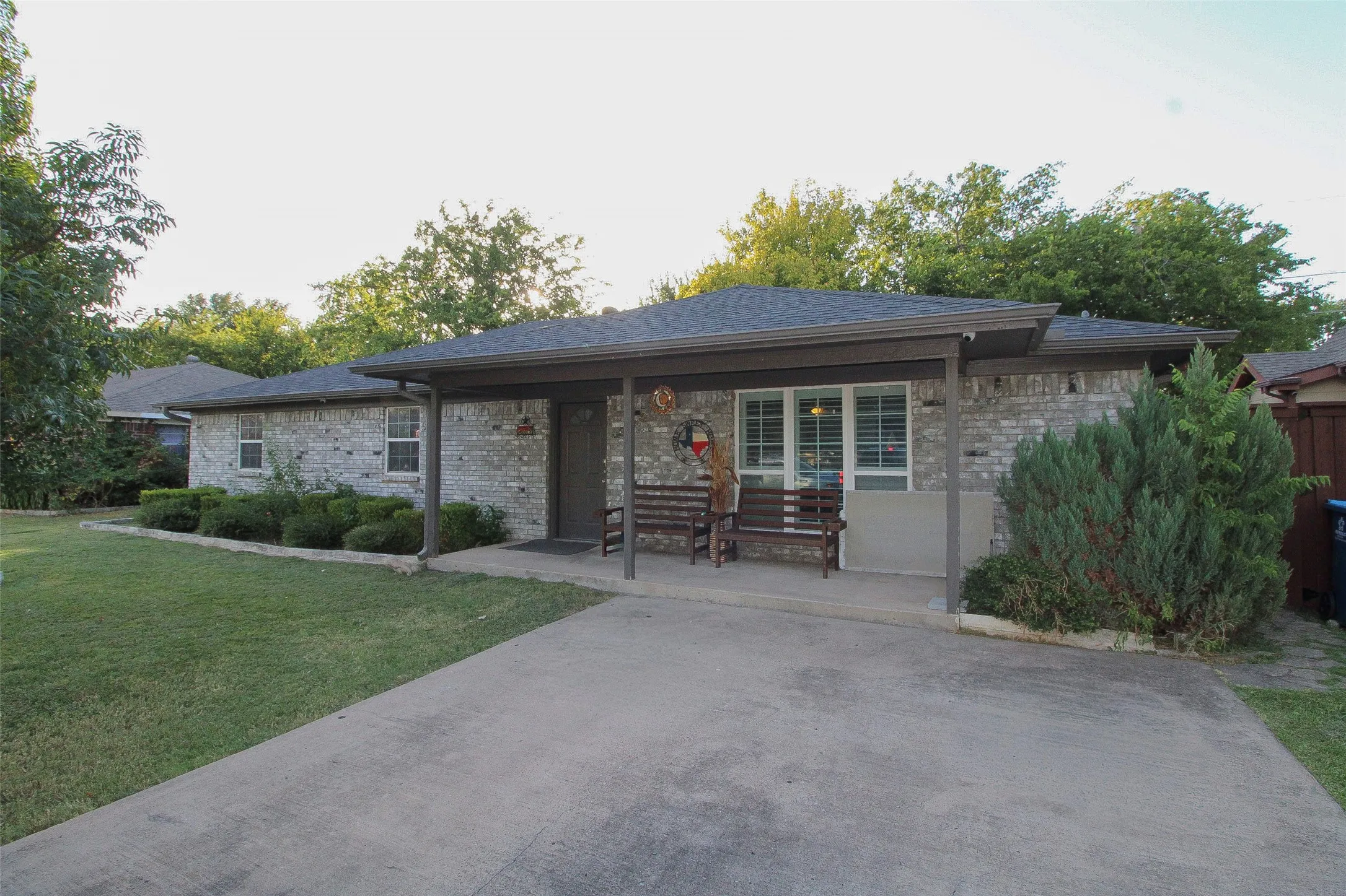 Grey brick exterior with a dark shingle roof, covered entry, and concrete driveway