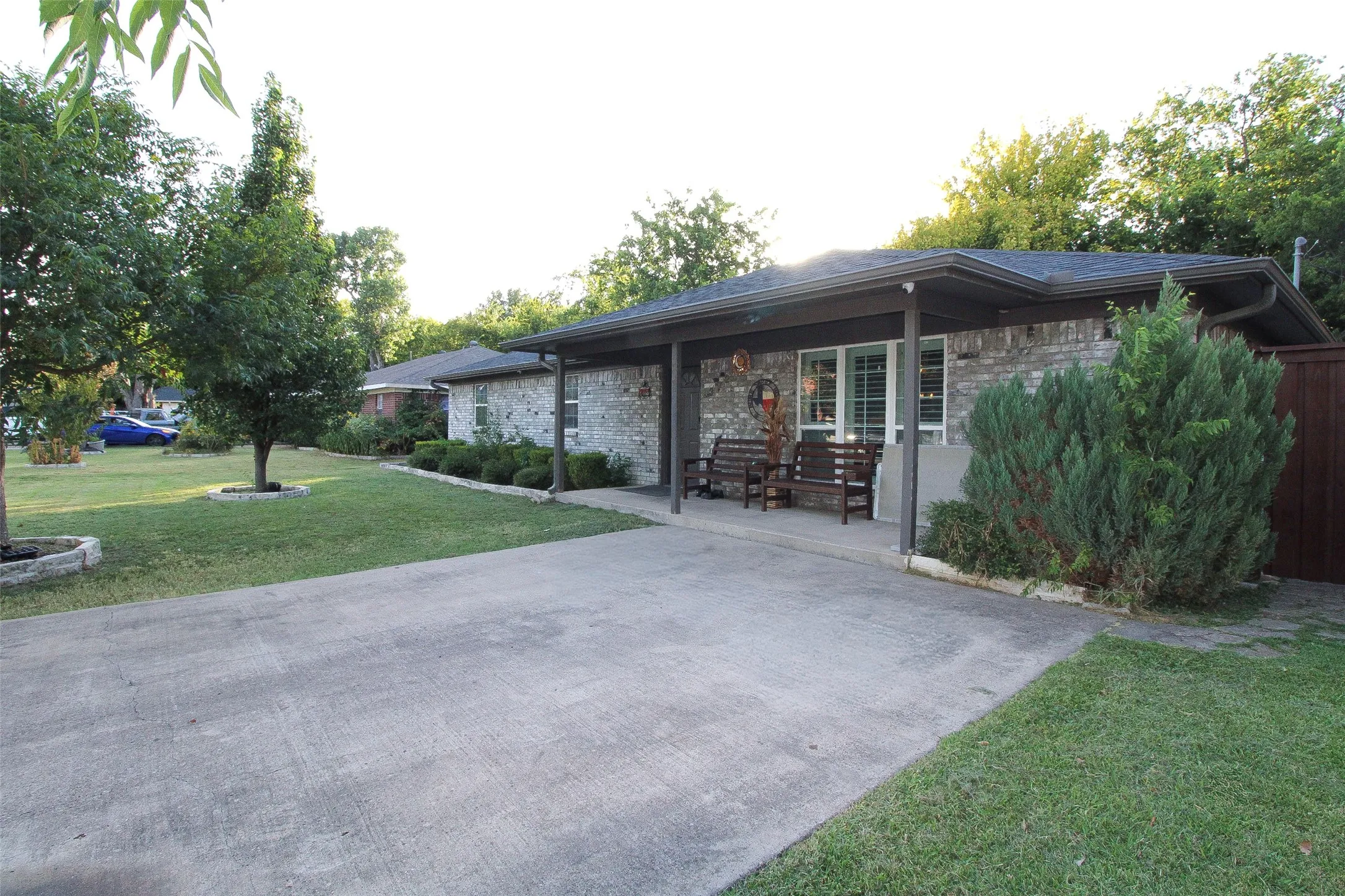 Brick exterior with covered front entry, mature landscaping, and an expansive driveway