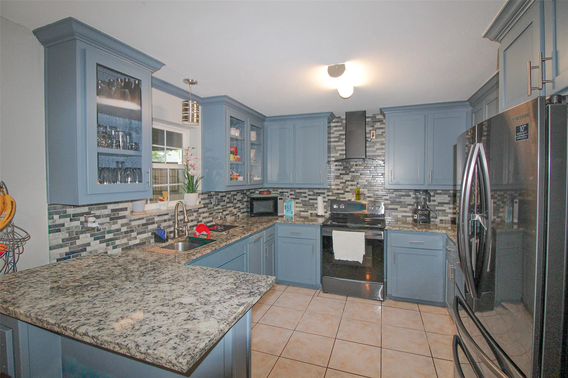 Kitchen featuring blue cabinetry, stone-finish countertops, mosaic tile backsplash, and stainless steel appliances