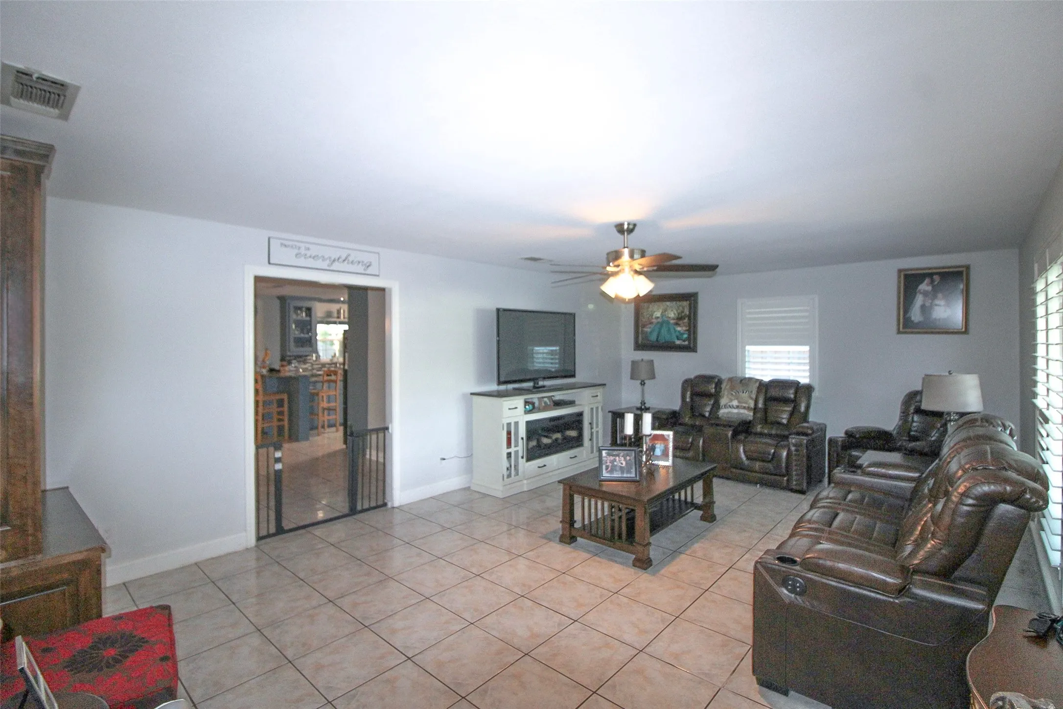Neutral wall tones, ceramic tile flooring, ceiling fan with integrated lighting, and window with plantation shutters