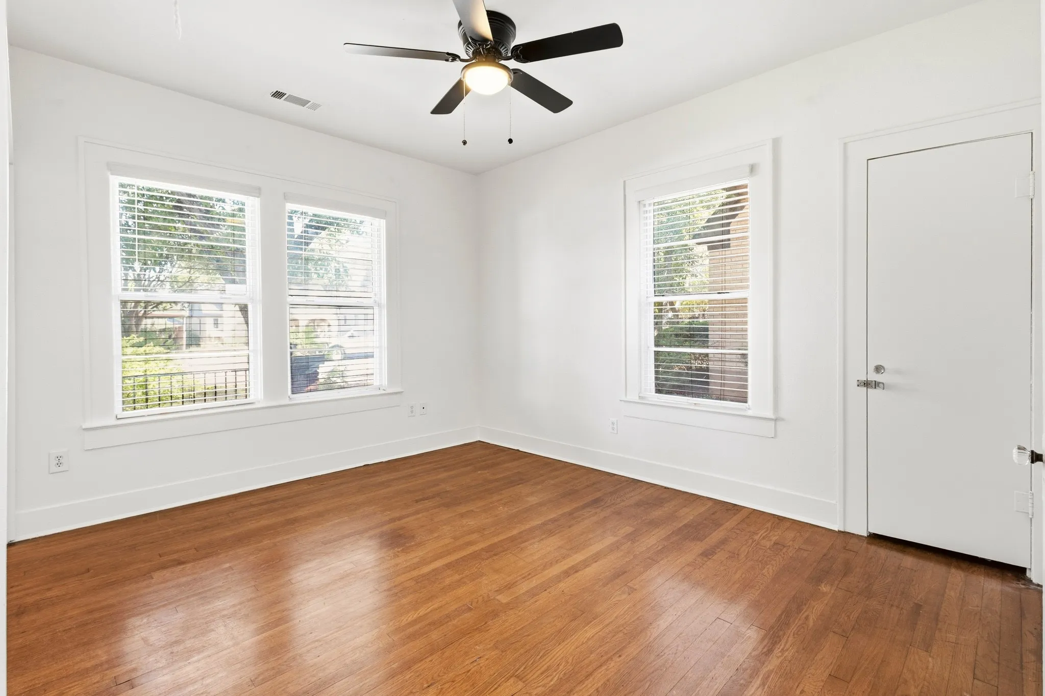 Hardwood flooring, two windows with blinds, a ceiling fan, and a white interior door