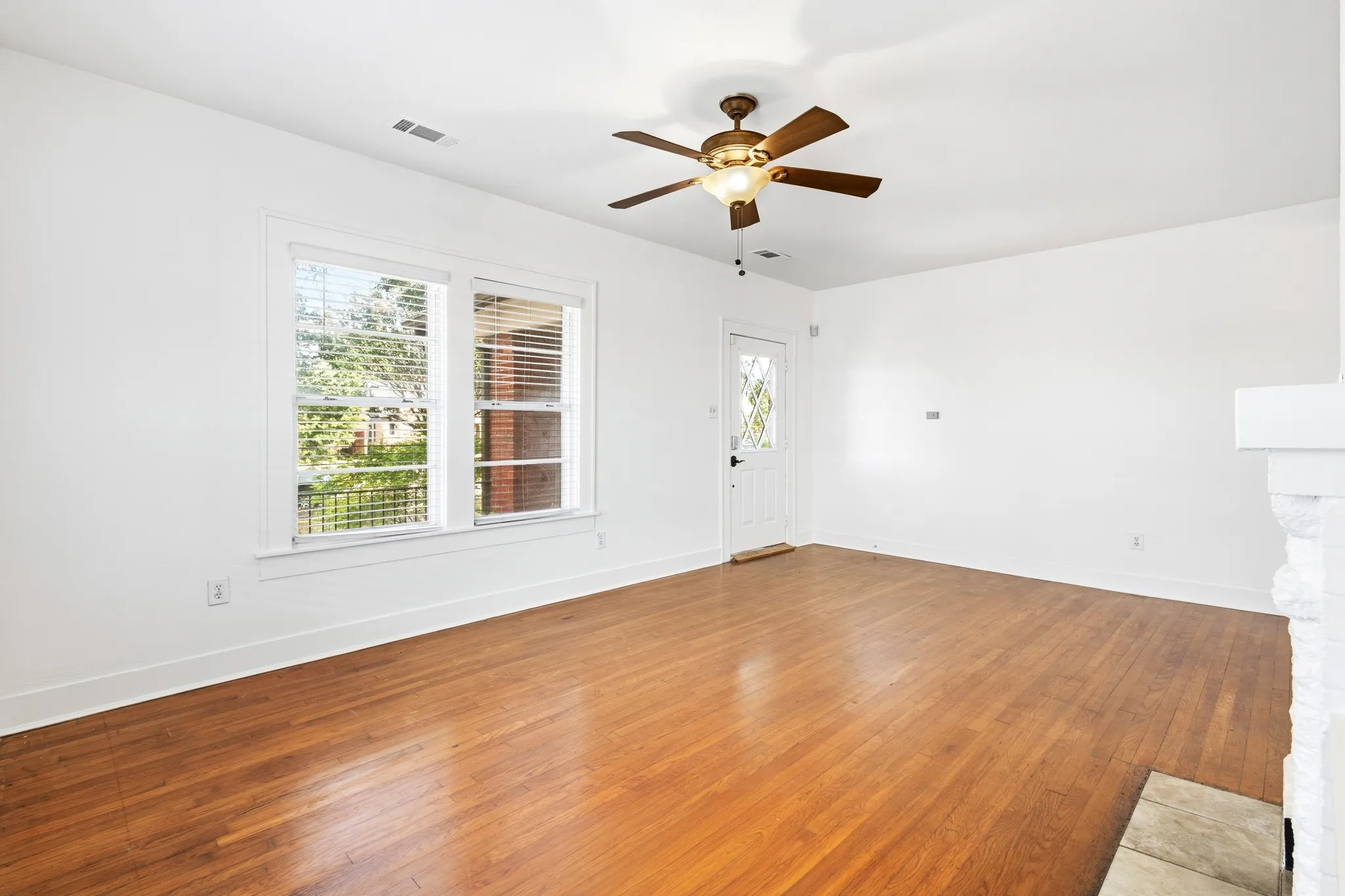 Wood-finish flooring, white painted walls, multi-pane windows with blinds, ceiling fan with integrated lighting, and a white entry door with decorative glass