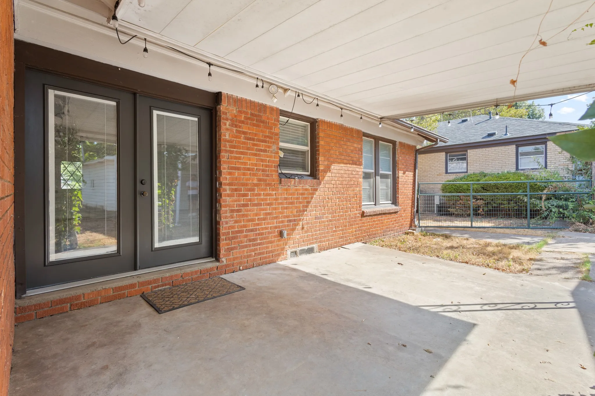 Covered concrete patio featuring brick exterior and black-framed double glass doors