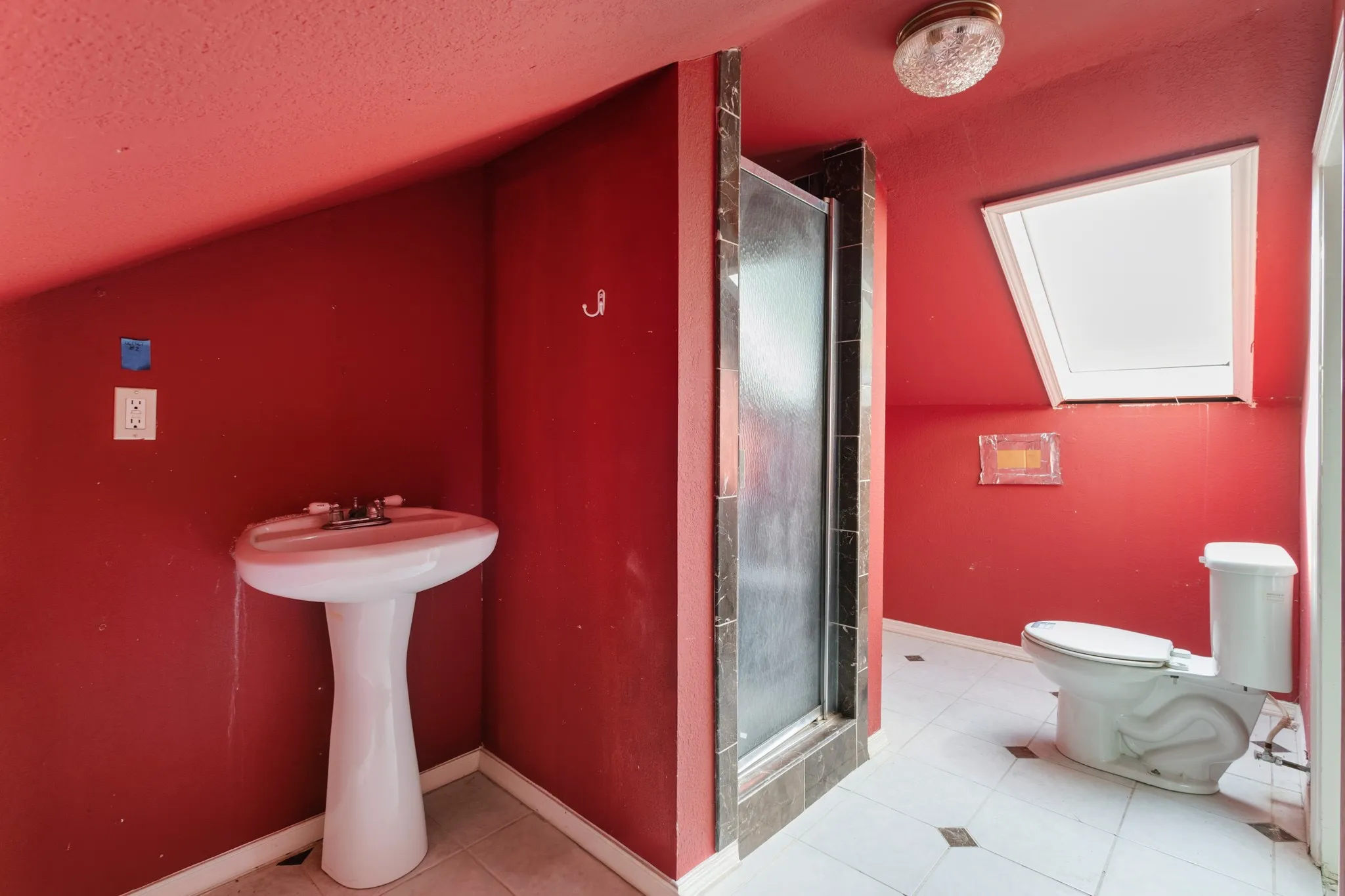 Pedestal sink, enclosed shower stall, toilet, skylight, and tiled flooring