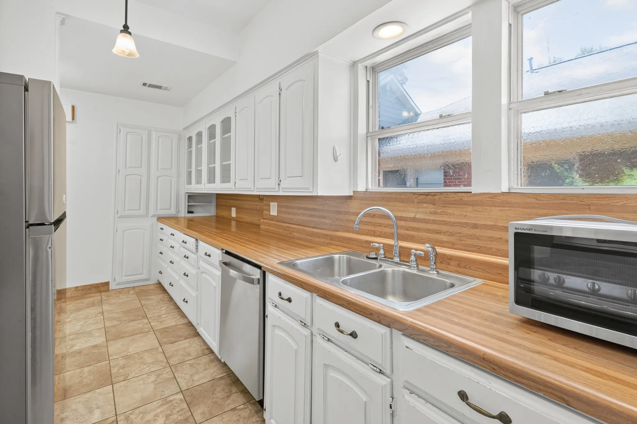 White cabinetry with glass-front accents, wood-finish countertops, and a dual stainless steel sink
