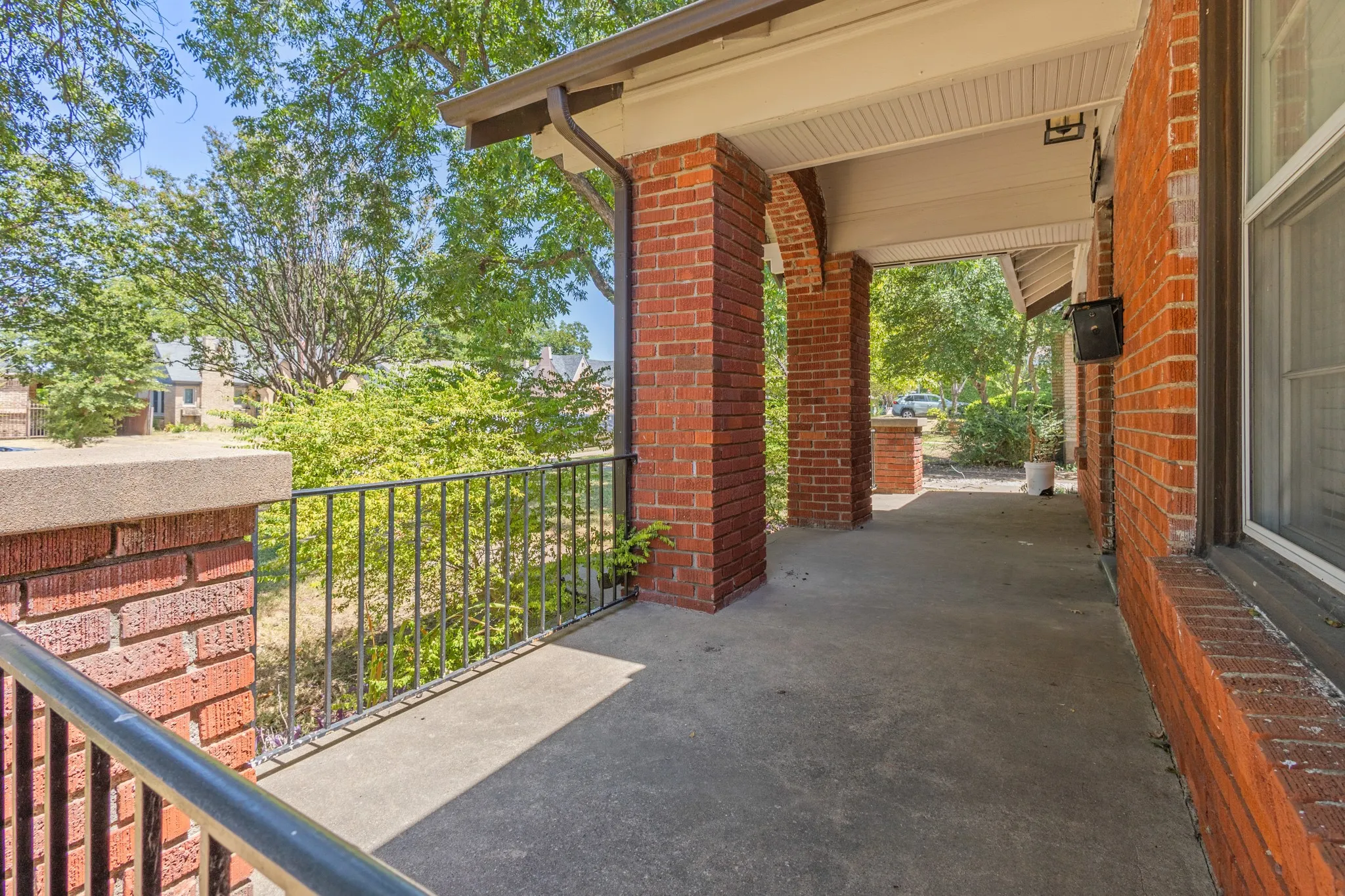 Brick exterior featuring a covered porch, concrete flooring, and metal railings