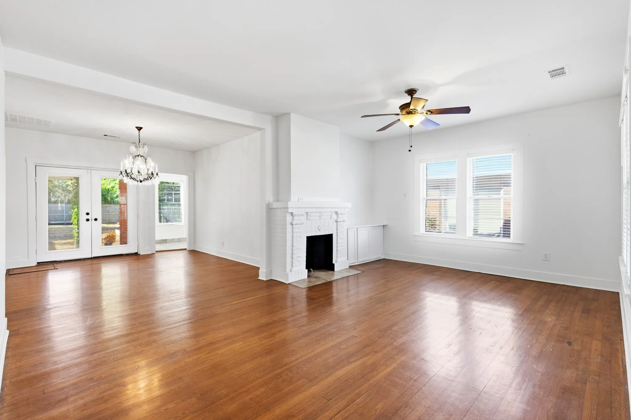 Wood-finish flooring, white walls, white brick fireplace, French doors, and a ceiling fan