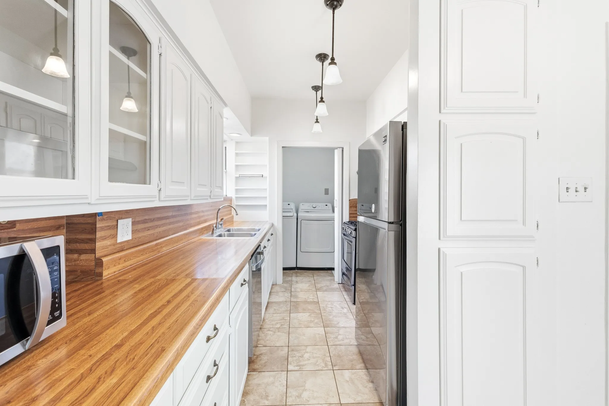 Galley kitchen featuring wood-finish countertops, white cabinetry, and stainless steel appliances