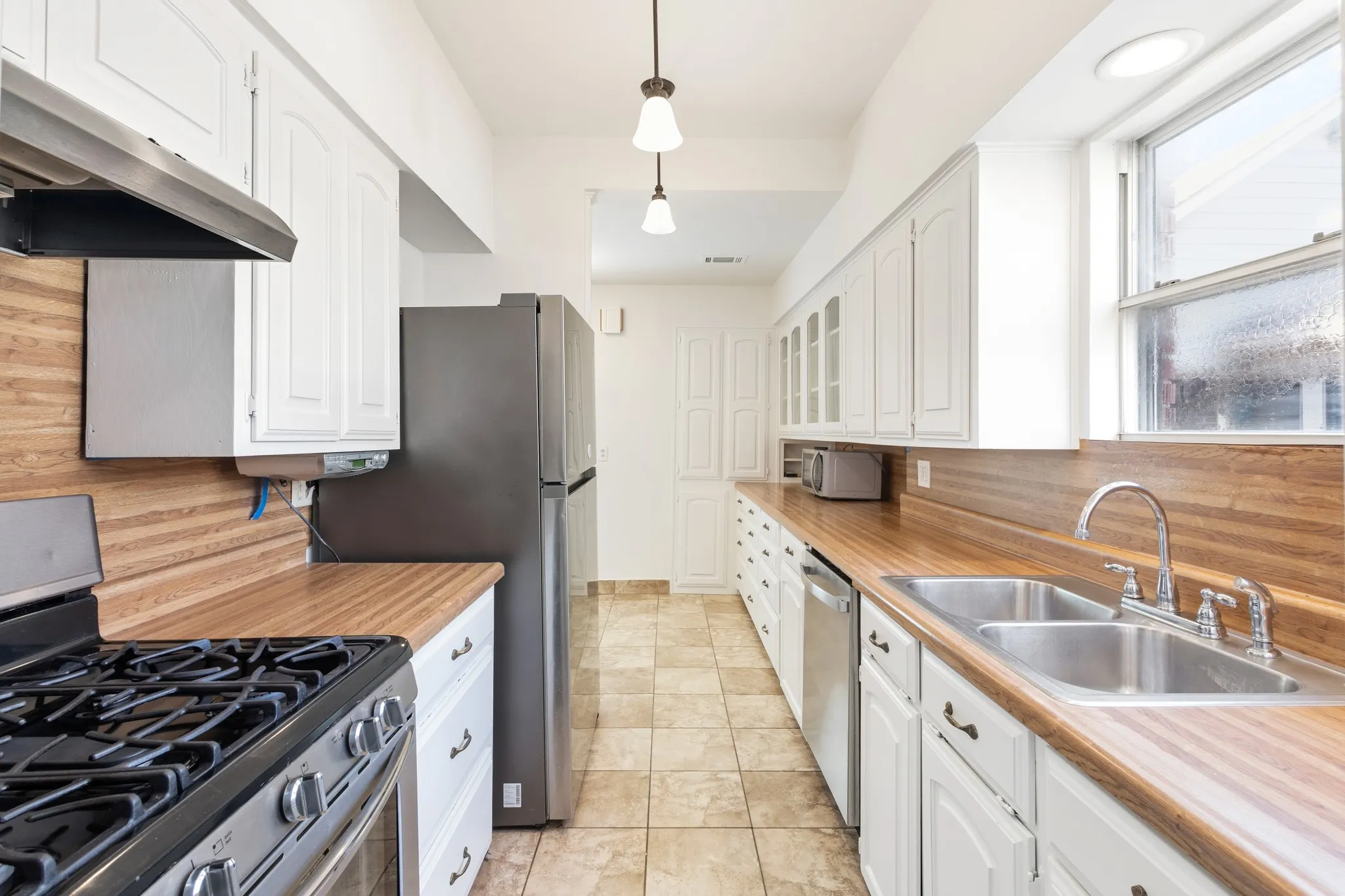 Galley kitchen featuring wood-finish countertops, white cabinetry, stainless steel appliances, and tile flooring