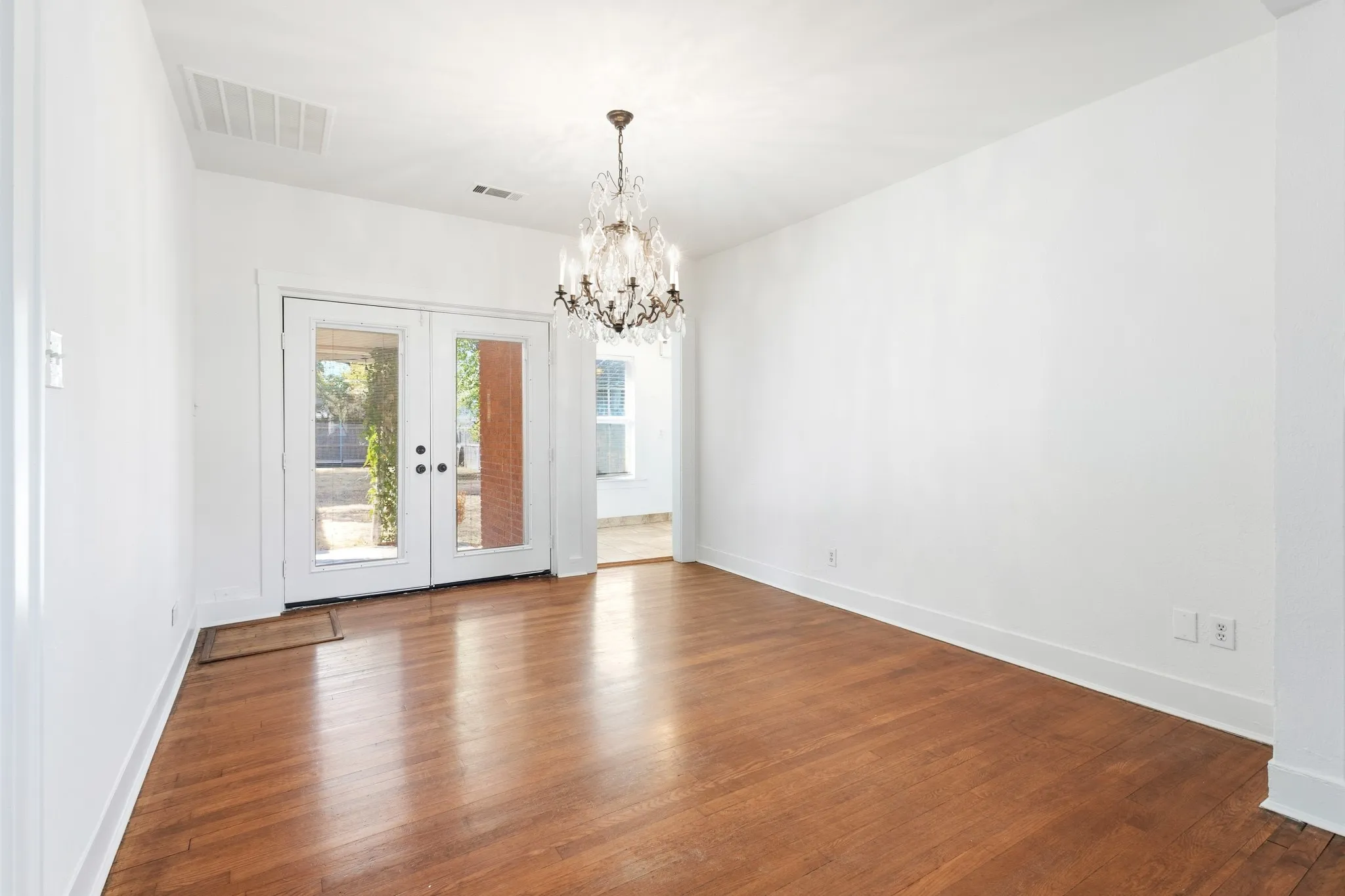 Hardwood flooring, crystal chandelier, double glass-paneled doors, and white walls