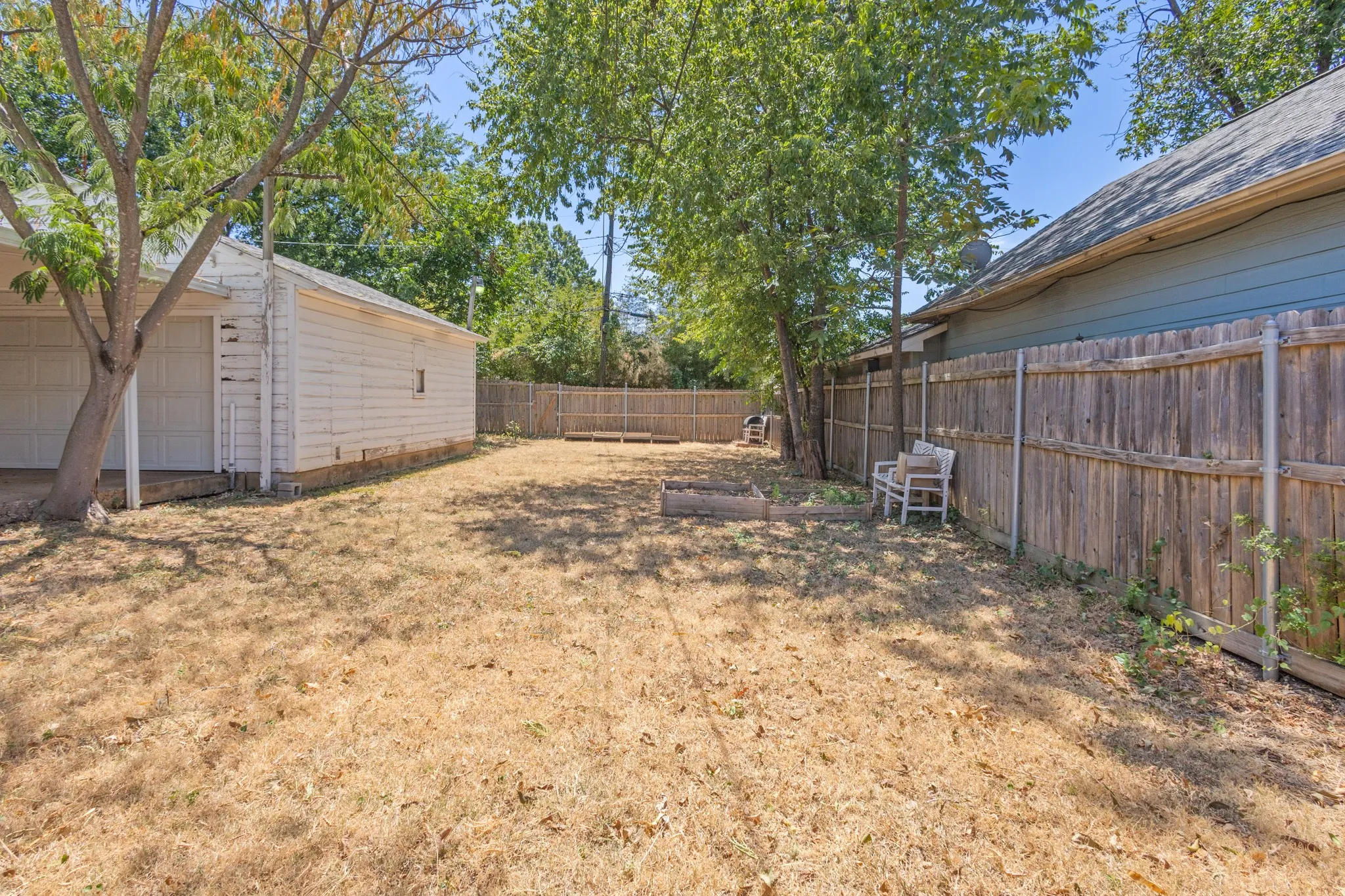Spacious backyard with a detached garage, wood privacy fencing, and mature trees