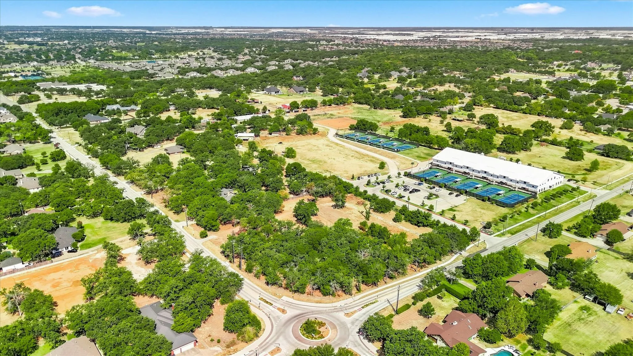 Expansive property featuring abundant mature trees, paved roads, and a clear blue sky