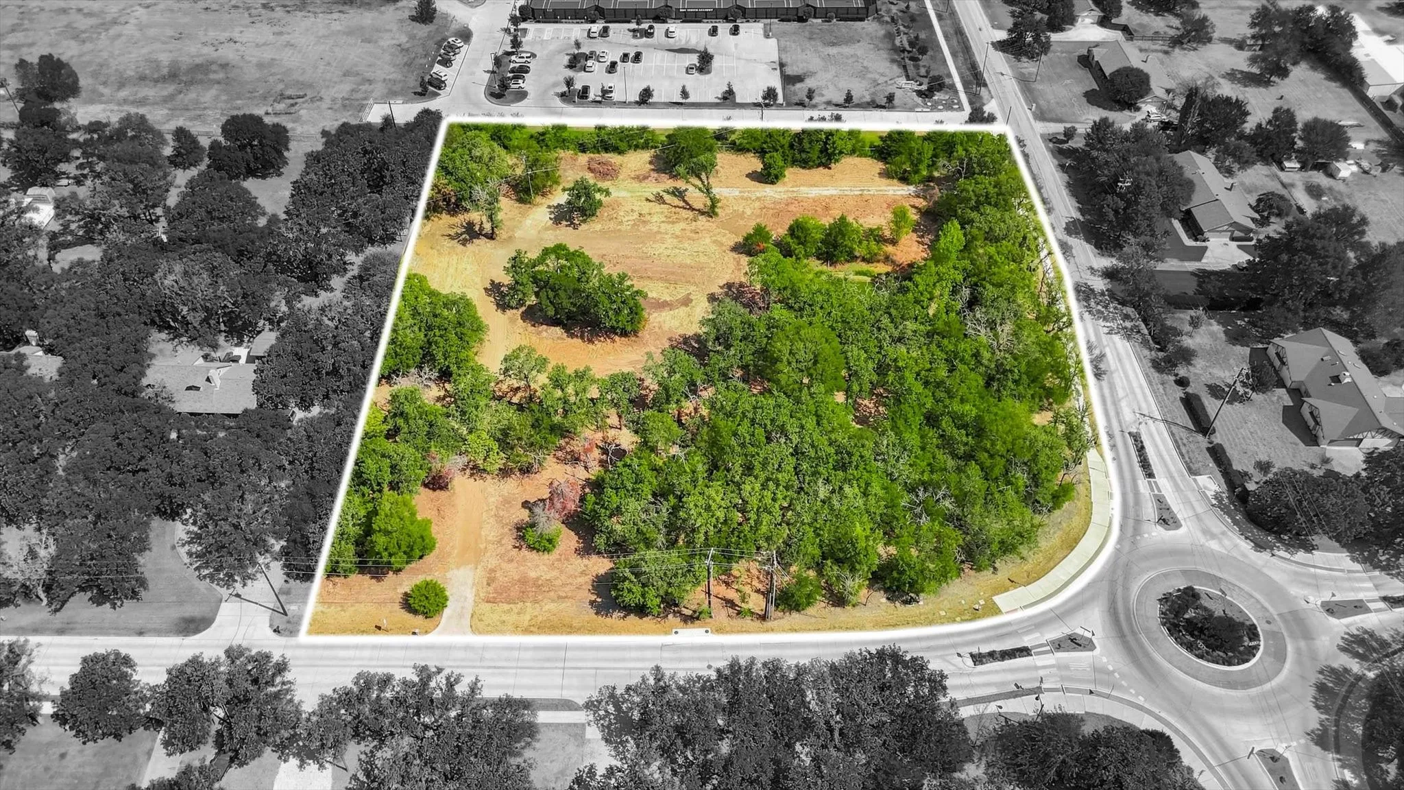 Expansive corner parcel featuring mature trees and clearings, bordered by paved roads and a roundabout