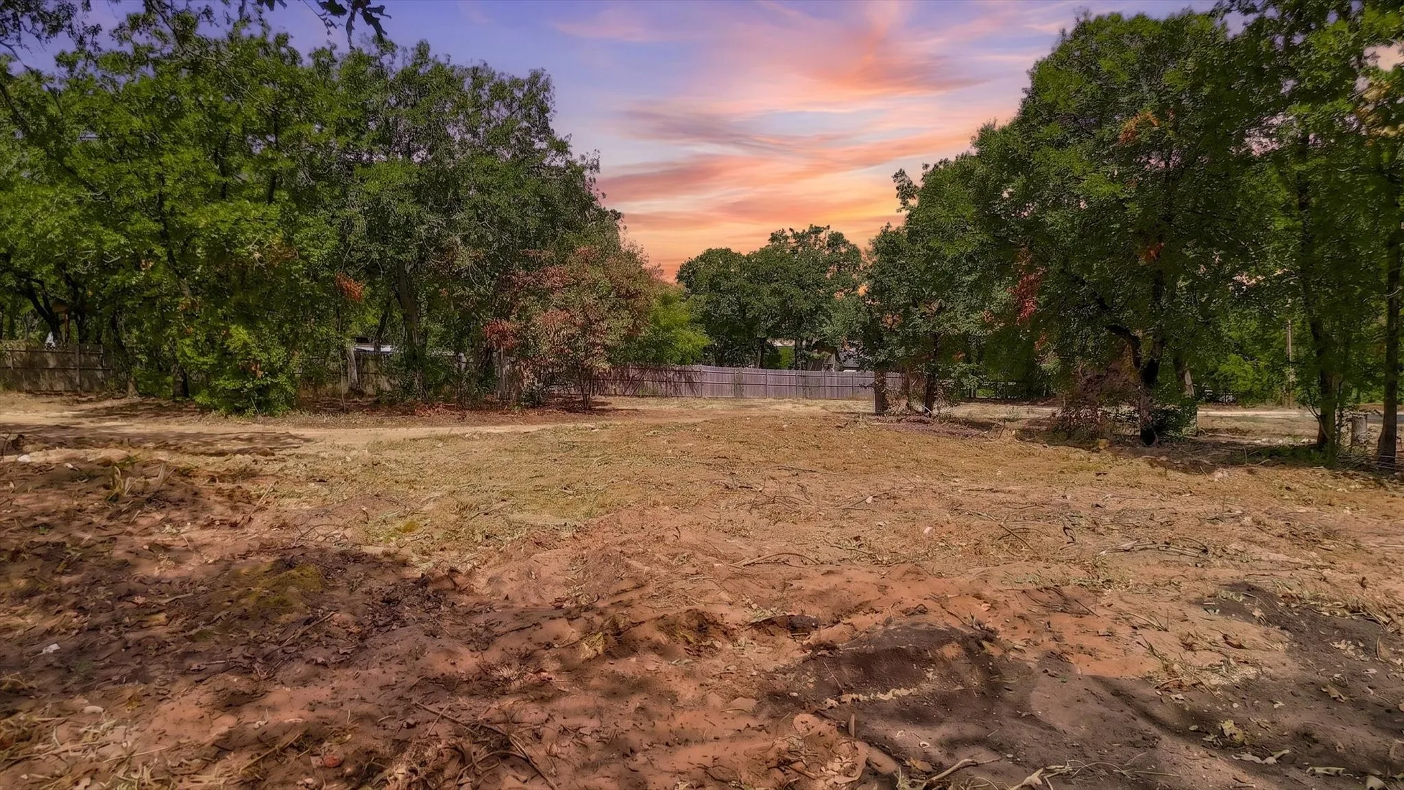 Cleared lot with mature trees and perimeter fencing