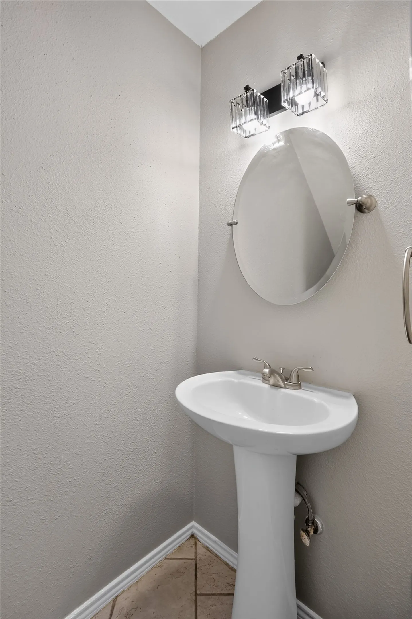 Pedestal sink with a brushed nickel faucet, an oval wall-mounted mirror, and a two-light vanity fixture with clear glass shades