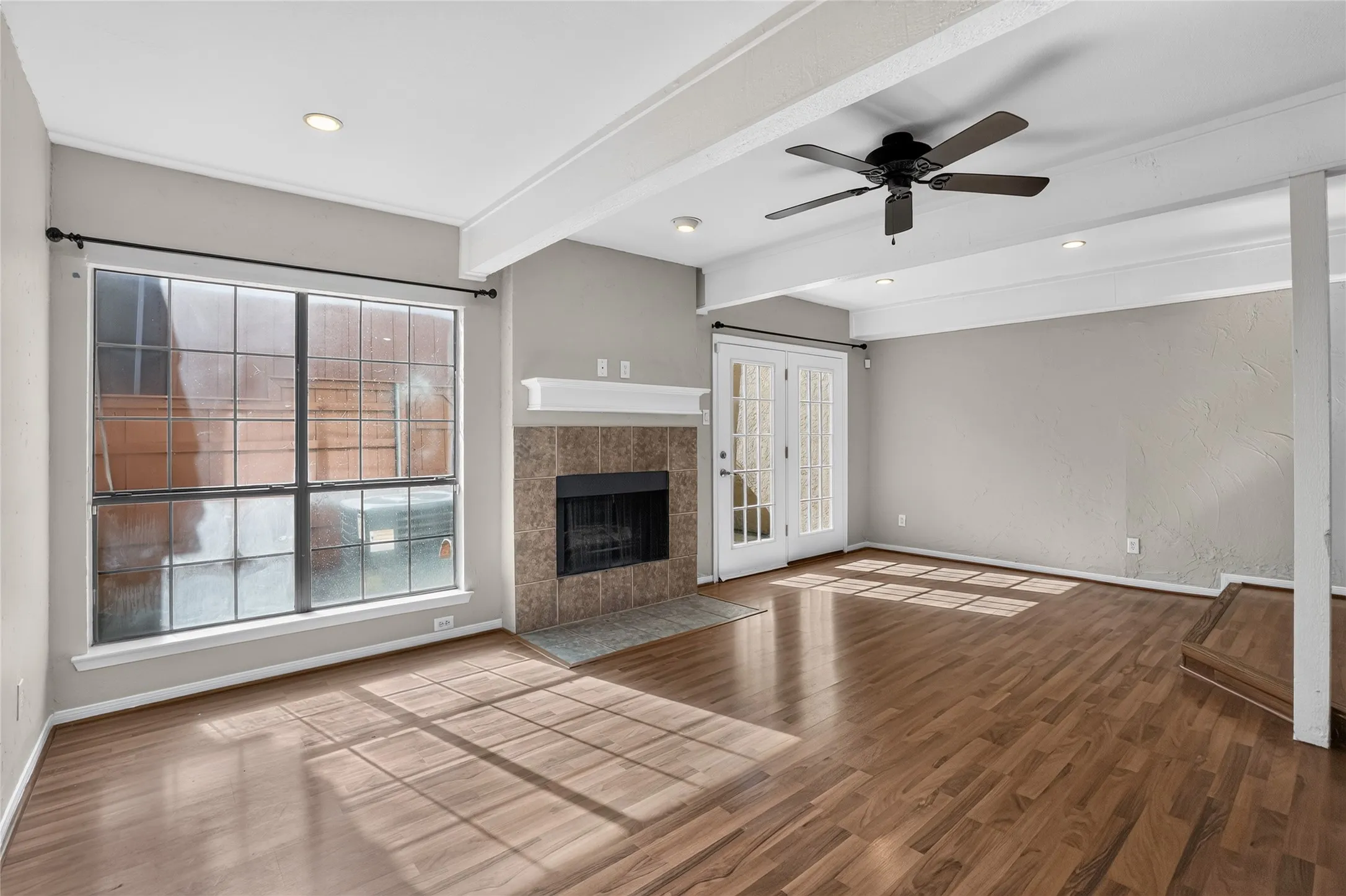 Hardwood-style flooring throughout, featuring a fireplace with tile surround, white mantel, and double French doors with interior grilles