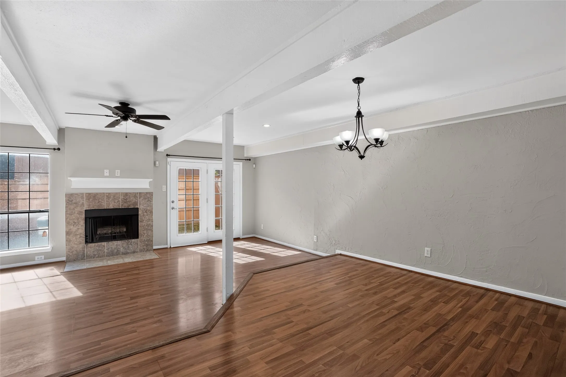 Spacious living area featuring wood-finish flooring, a tiled fireplace with a white mantel, and a ceiling fan