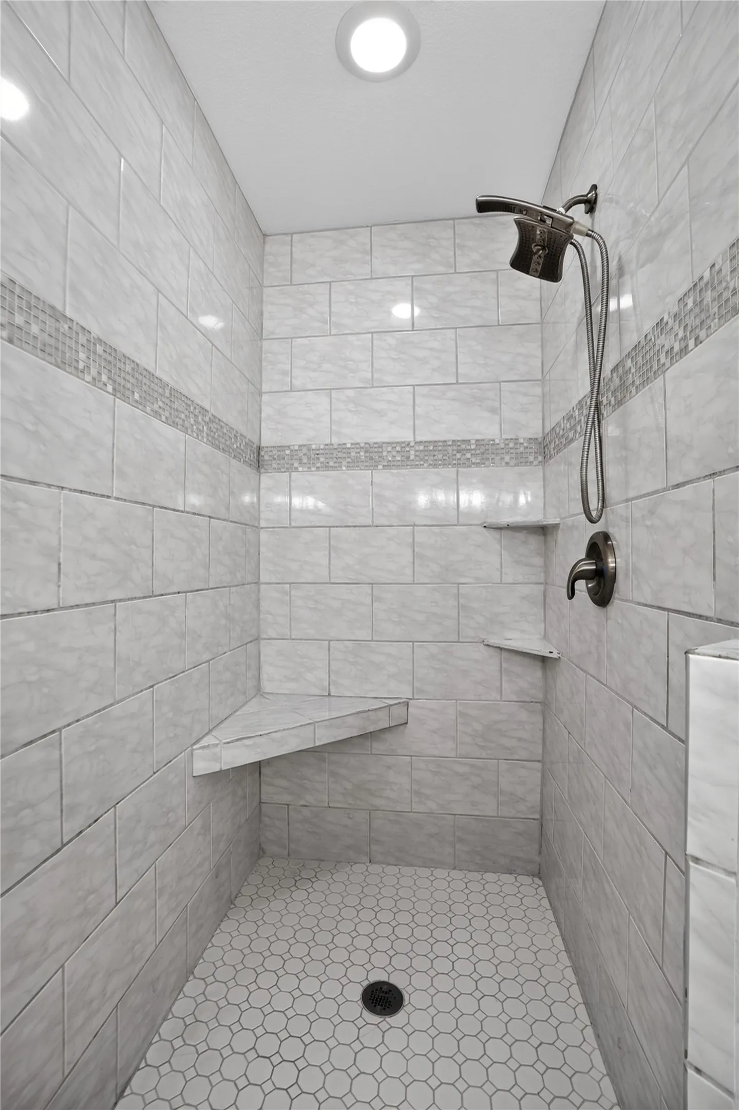 Tiled shower enclosure featuring a mosaic accent band, integrated corner shelving, and a built-in bench seat