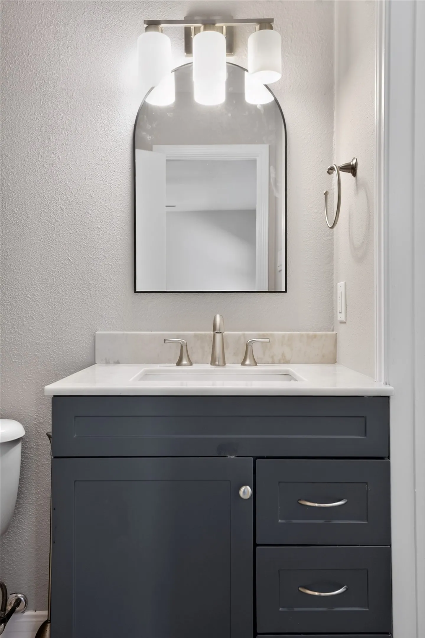 Vanity with a white countertop and integrated sink, a brushed nickel faucet, a dark blue cabinet with storage, and a decorative arched mirror