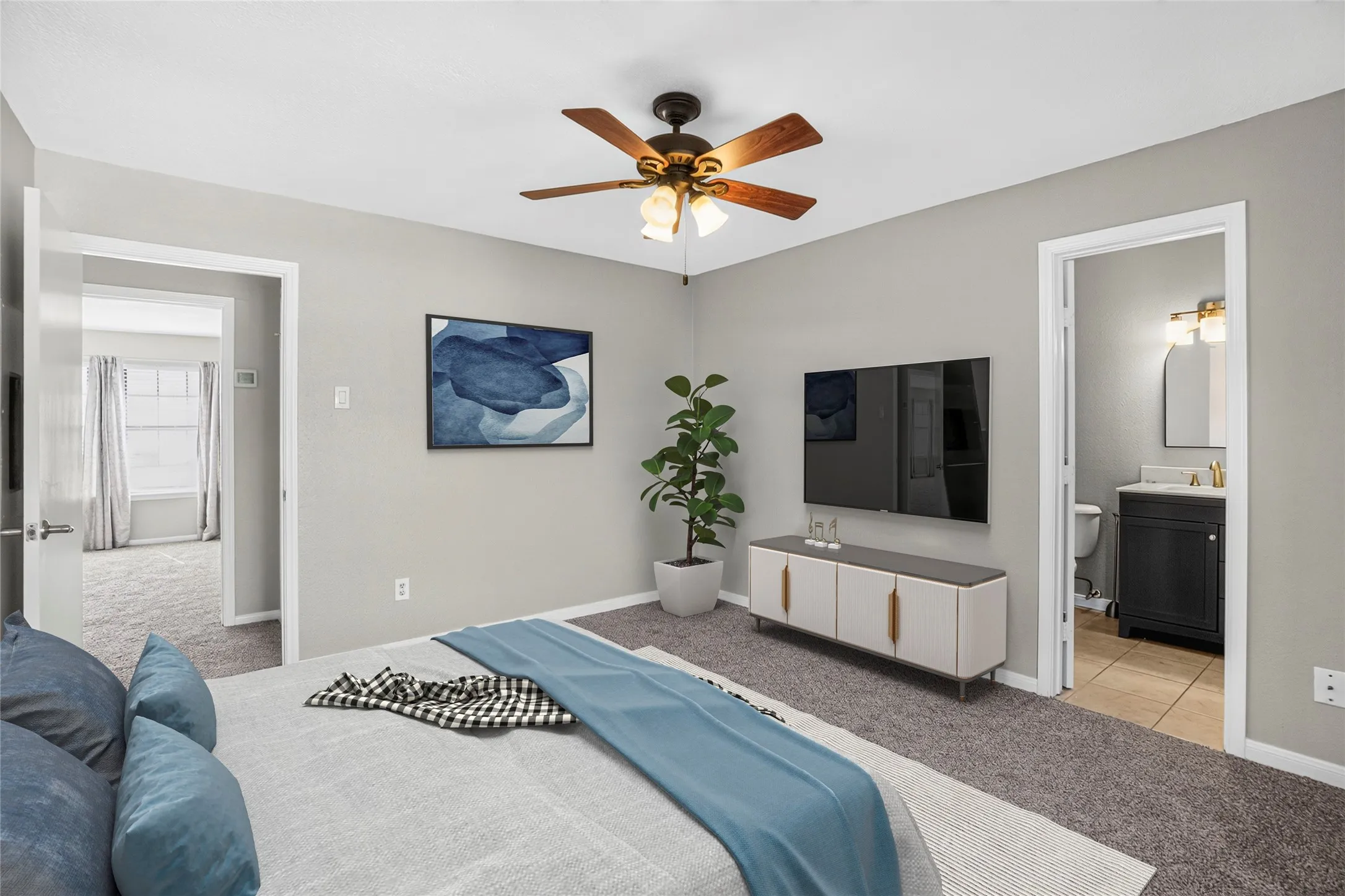 Carpeted room with a ceiling fan, wall-mounted television, and an attached full bathroom featuring a vanity with a dark cabinet and a wall-mounted light fixture