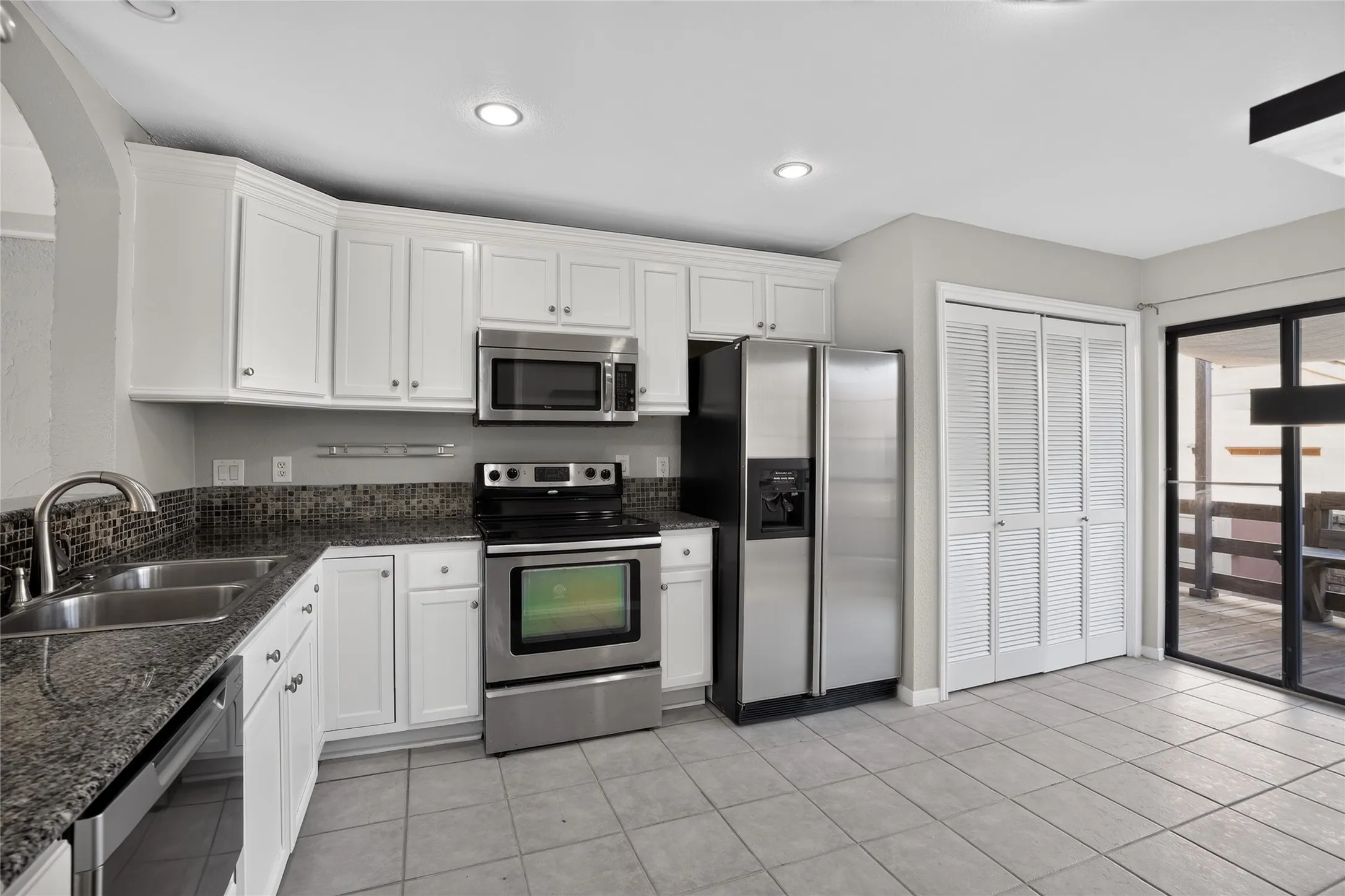 Kitchen featuring white cabinetry, stainless steel appliances, dark speckled countertops, and a mosaic tile backsplash