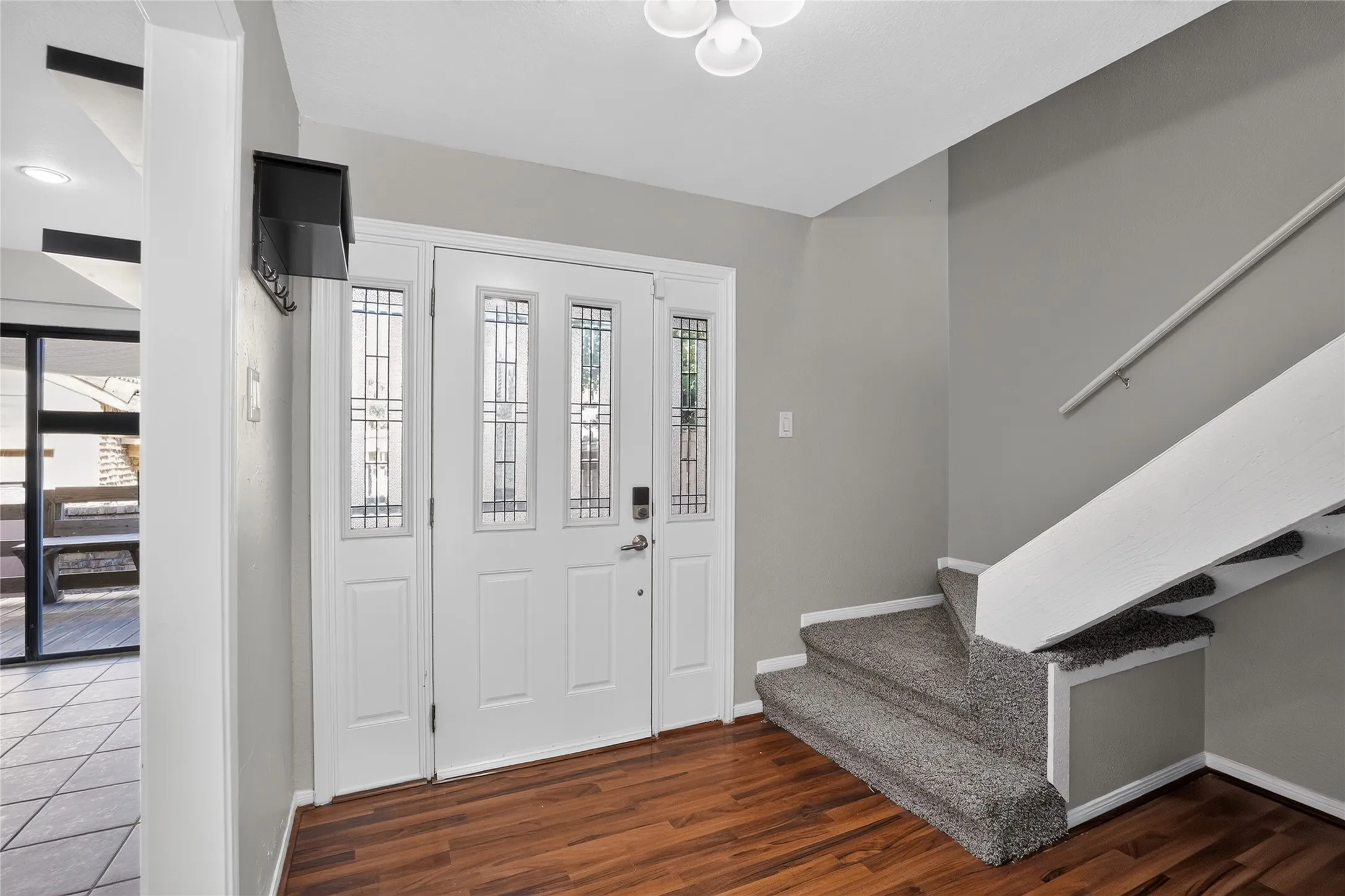 Entryway featuring wood-finish flooring, a white paneled entry door with sidelights, a textured carpeted staircase, and a white handrail