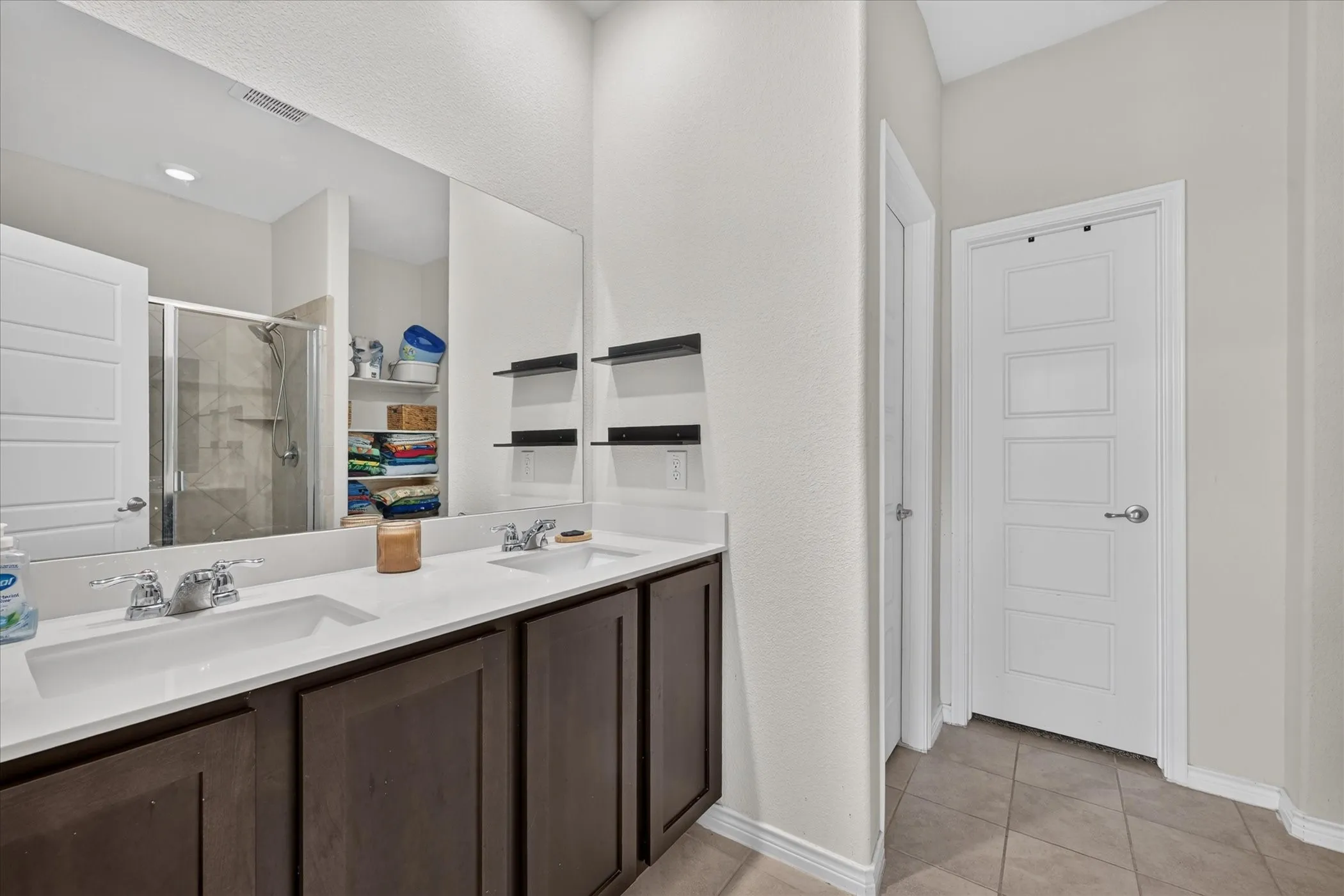 Dual basin vanity with solid surface countertop, dark wood-finish cabinetry, and chrome fixtures