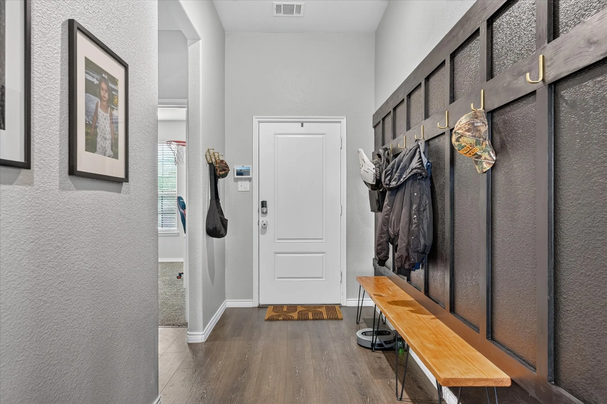 Entryway featuring wood-finish flooring, a white paneled door, and a built-in wall-mounted coat rack with a wood bench