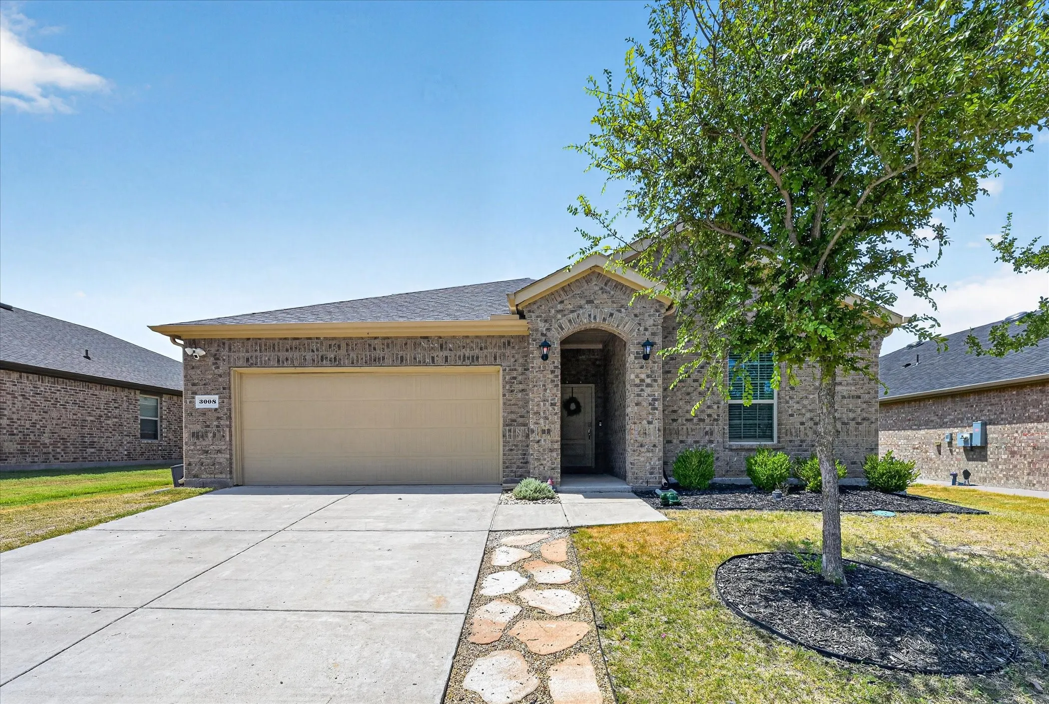 Brick exterior with an arched entryway, attached garage, concrete driveway, and stone-paver walkway