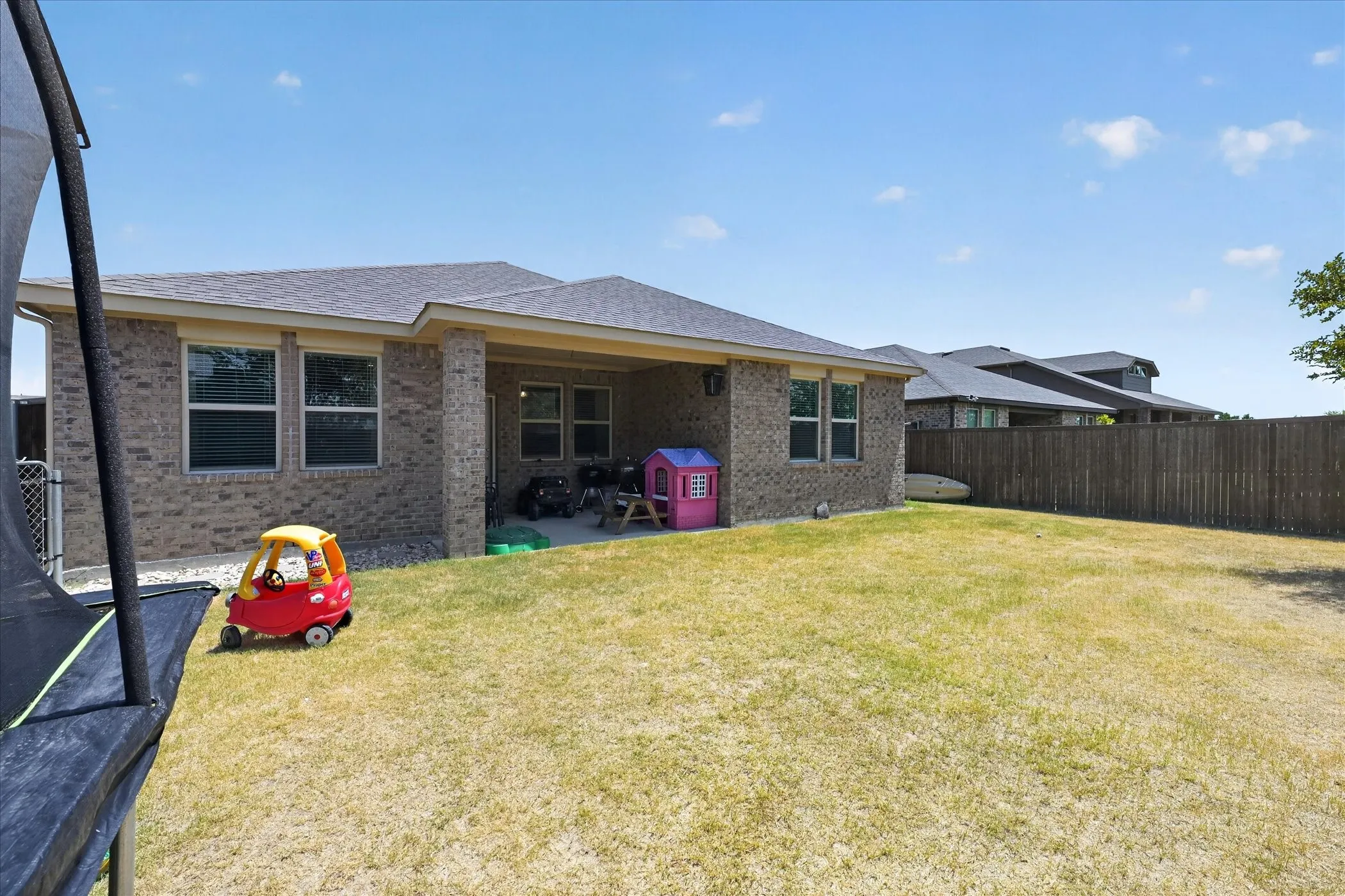 Expansive backyard featuring a manicured lawn, brick exterior, covered patio, and wood privacy fencing