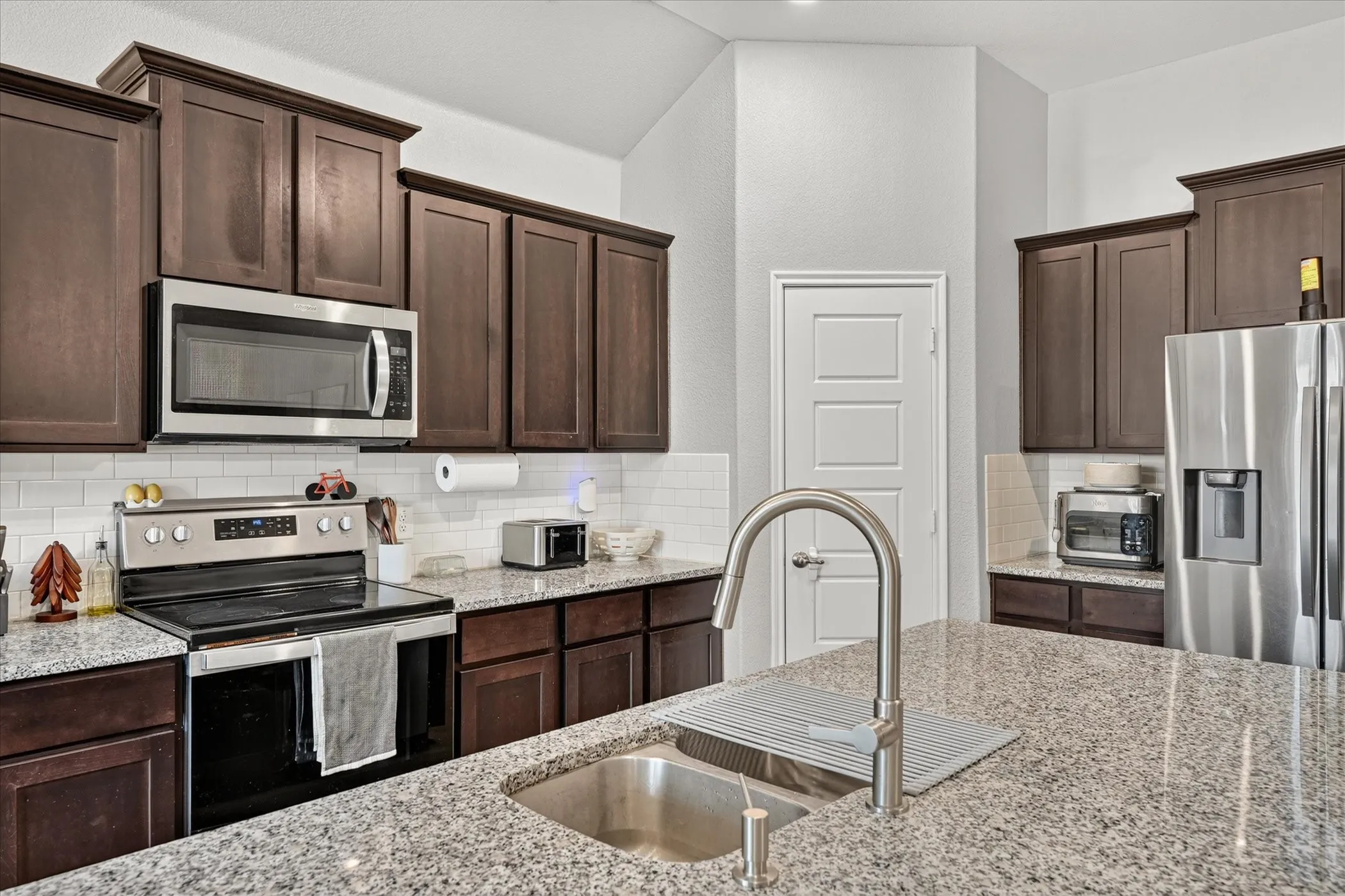 Kitchen featuring stainless steel appliances, dark wood-finish cabinetry, granite countertops, and a subway tile backsplash