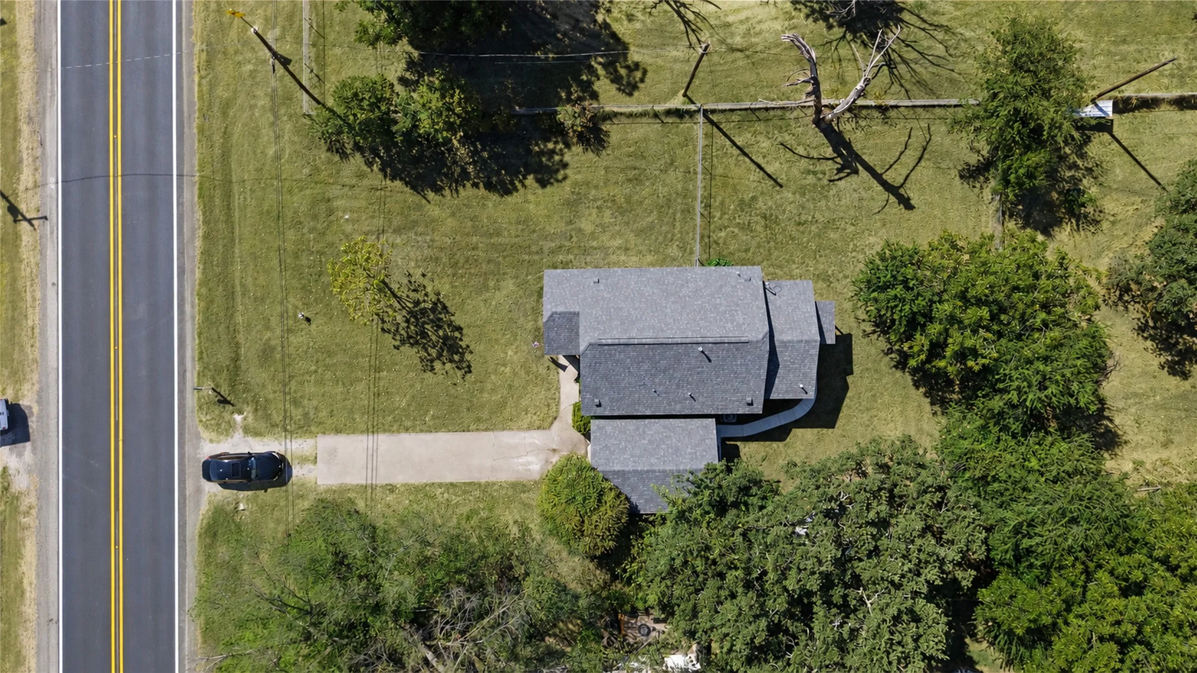 Pitched roofline residence with multiple sections, substantial front lawn, mature trees, and direct access to a paved road