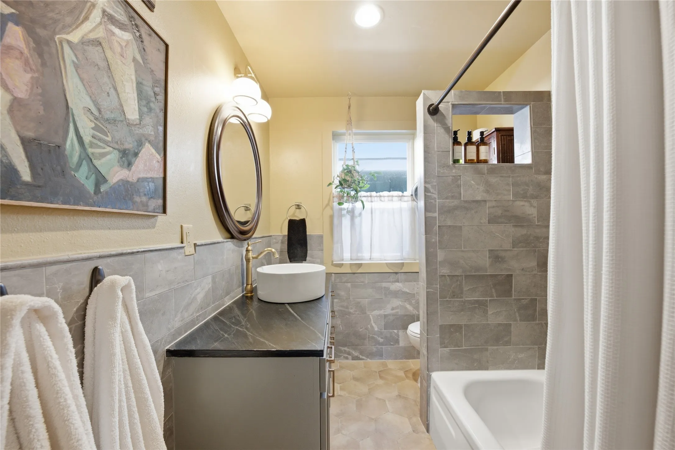 Modern vanity with a vessel sink, dark countertop, and brass-finish faucet