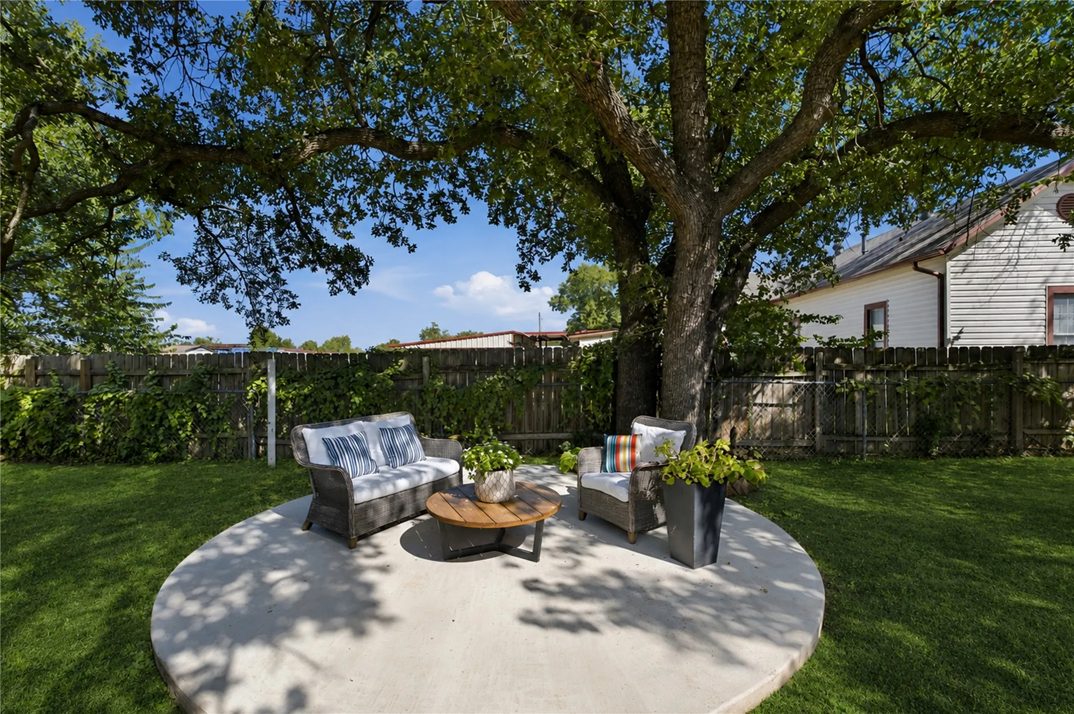 Expansive lawn featuring a mature tree, a circular concrete patio, and a wood privacy fence