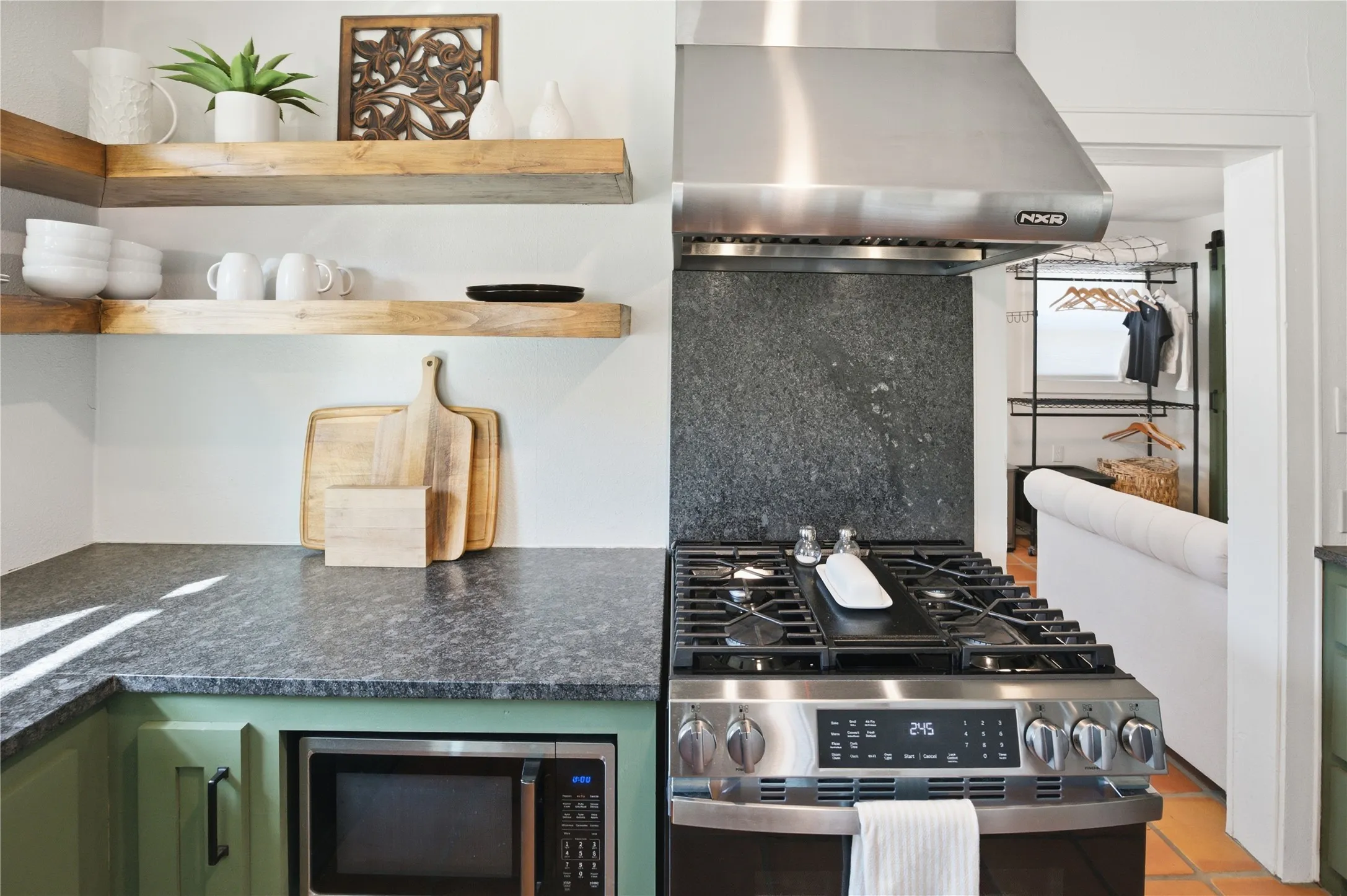 Stainless steel range with a coordinating hood, dark stone backsplash, and wood-finish open shelving